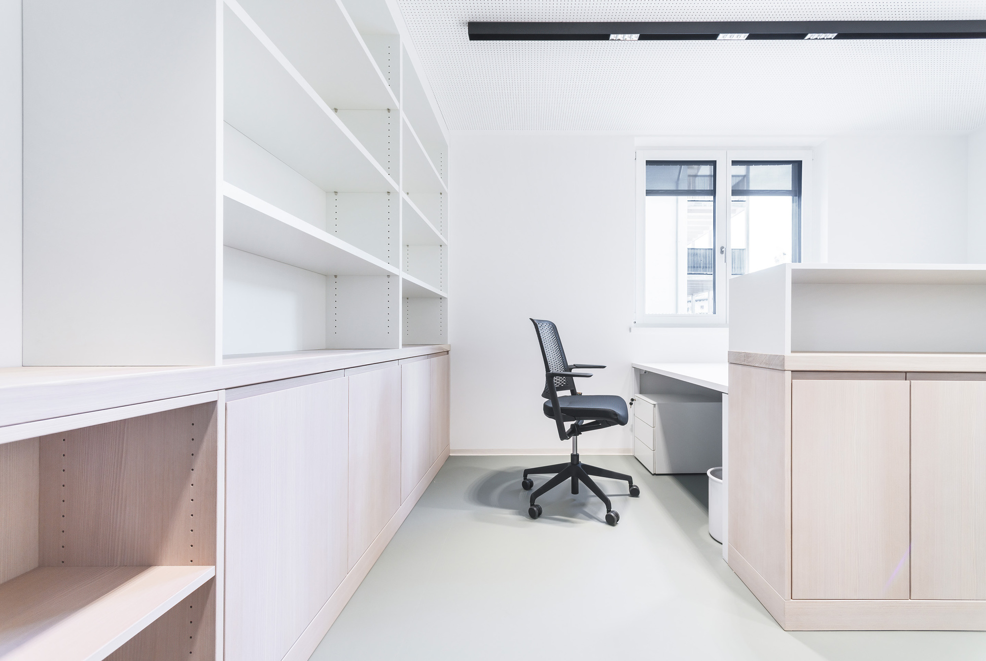 Individual workstation with white cabinetry and mesh office chair in narrow workspace with grey flooring