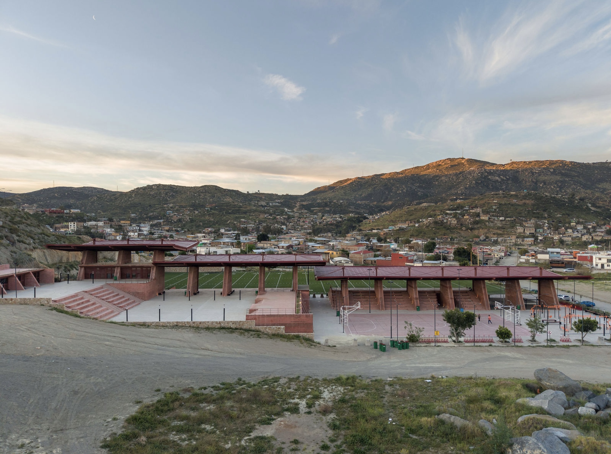 Distant view of the linear canopy structures spanning the athletic complex against hillside development