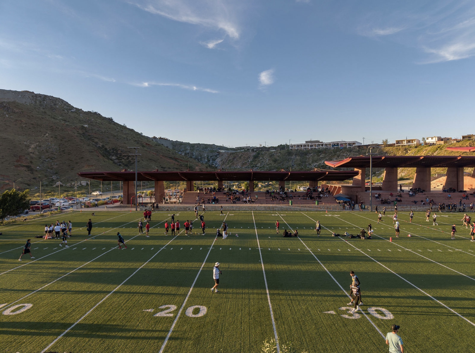 Football field with players practicing beneath the canopy and terraced seating in afternoon light