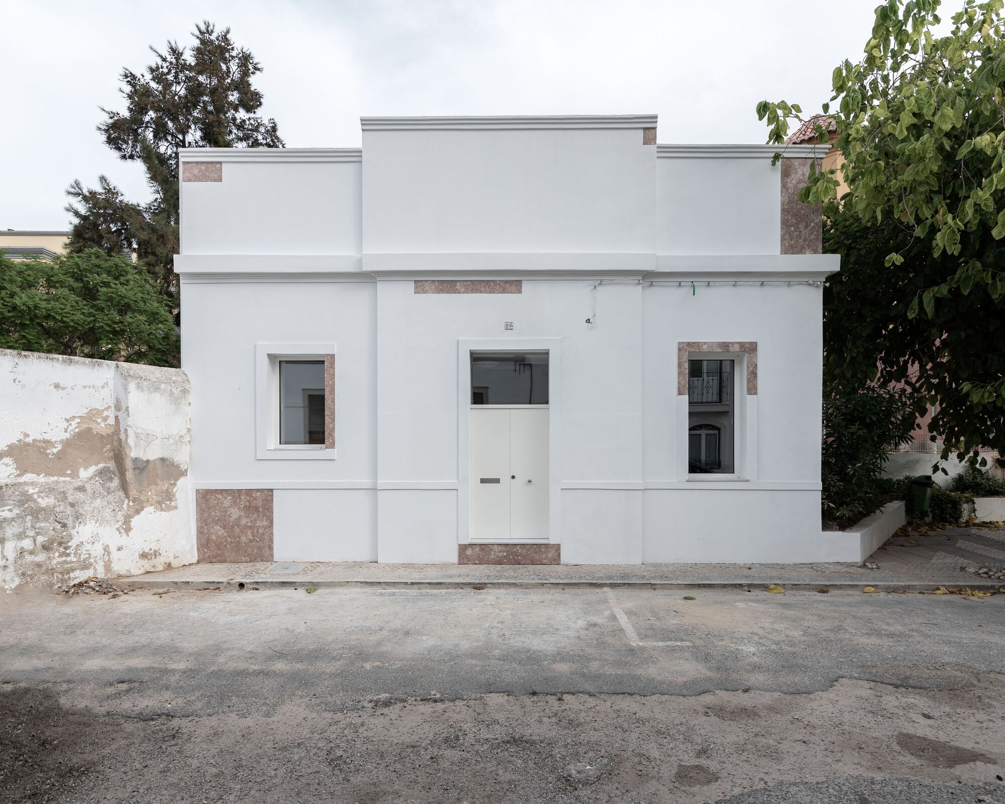 Street facade with white stucco walls and stone accents flanked by weathered perimeter walls and trees