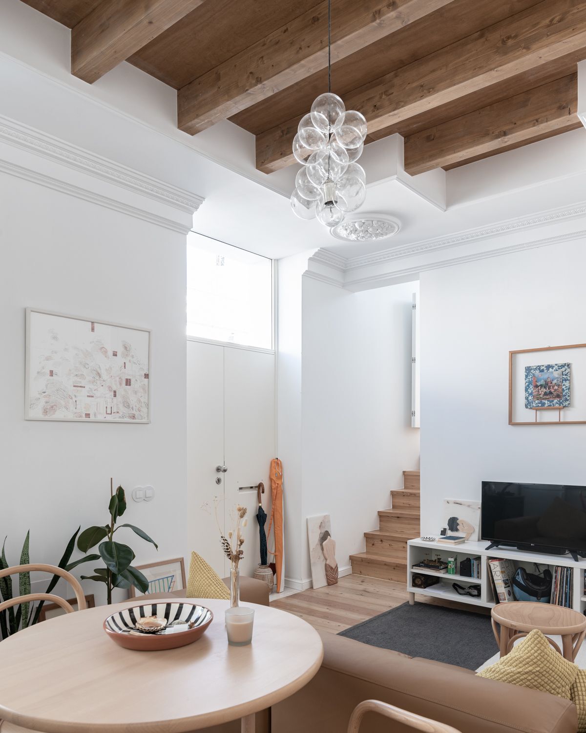 Double-height living space with exposed timber beams and a glass bubble chandelier over a dining table