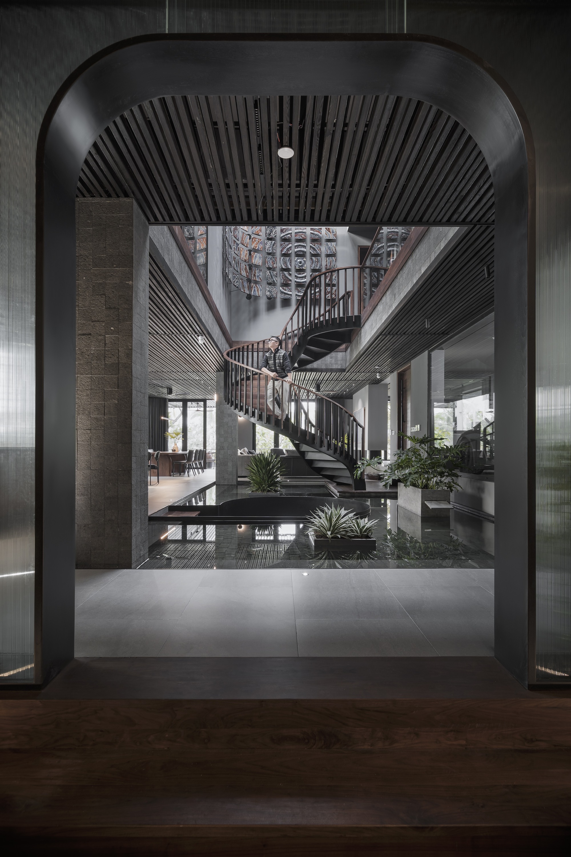 View through an arched threshold into the atrium space with spiral stair and slatted black ceiling