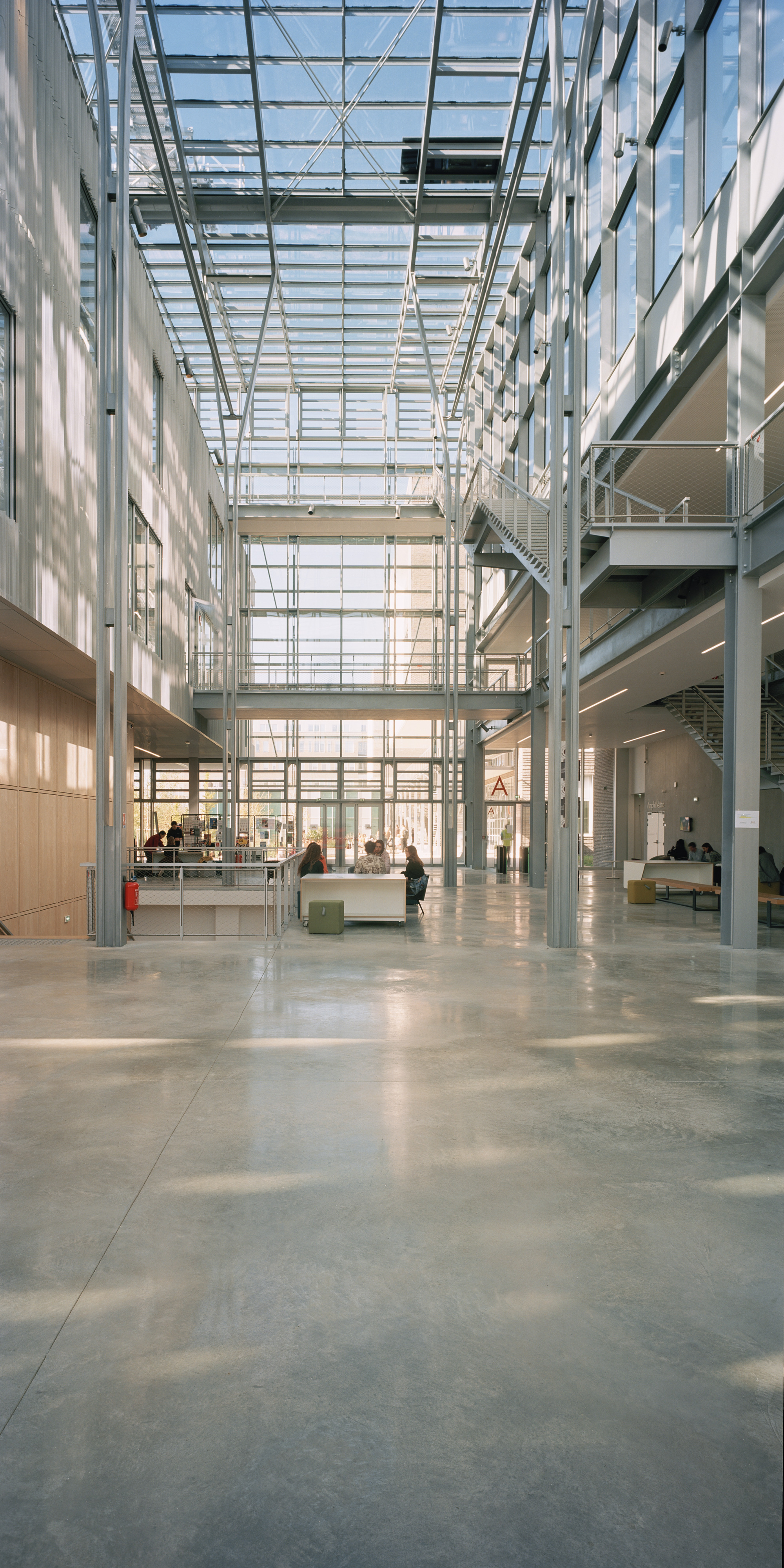 Interior atrium with glass roof structure and steel columns casting shadows on polished concrete floor