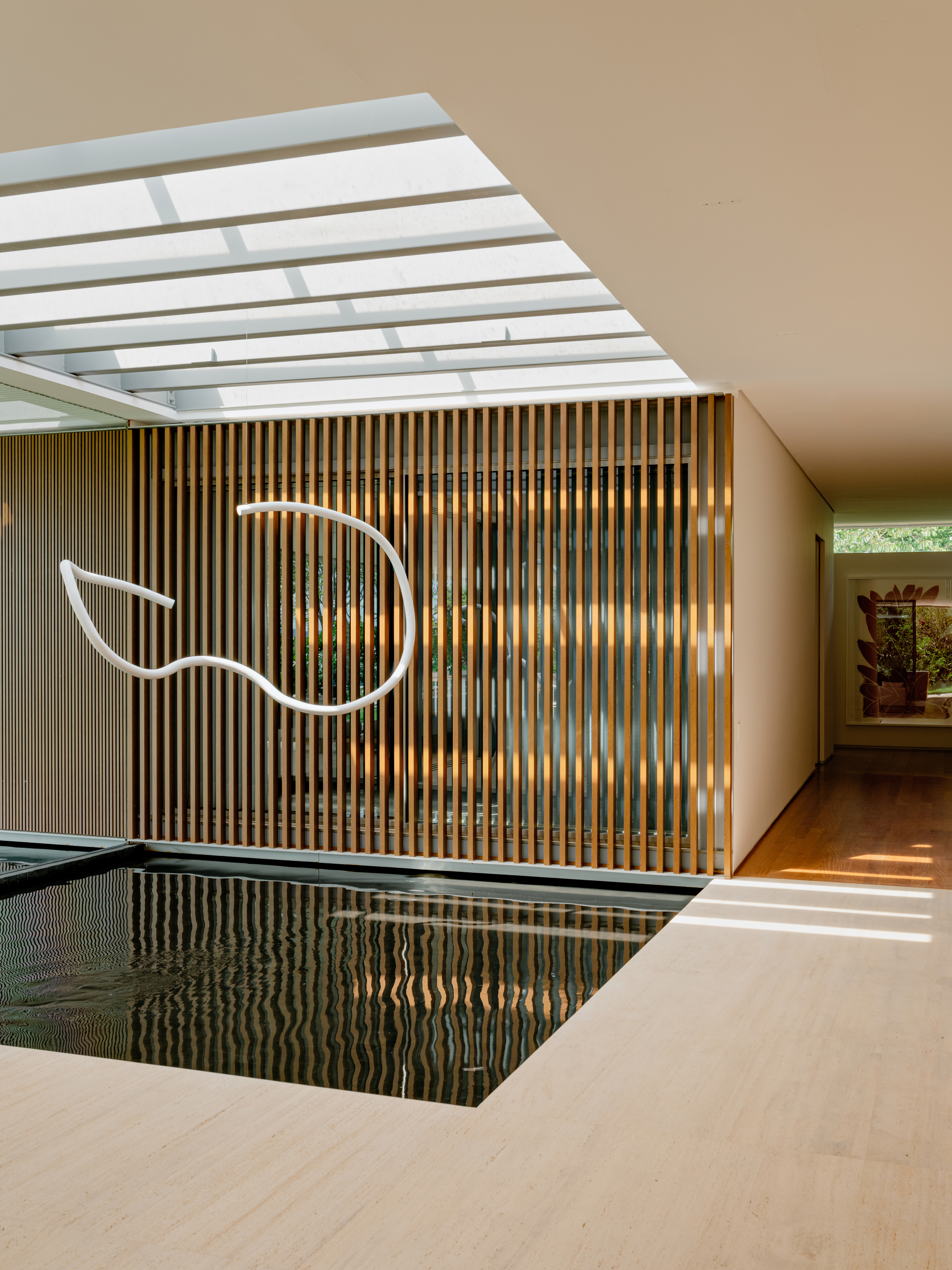 Indoor pool with timber slatted screen wall, striped skylight overhead, and a sculptural light fixture above the water