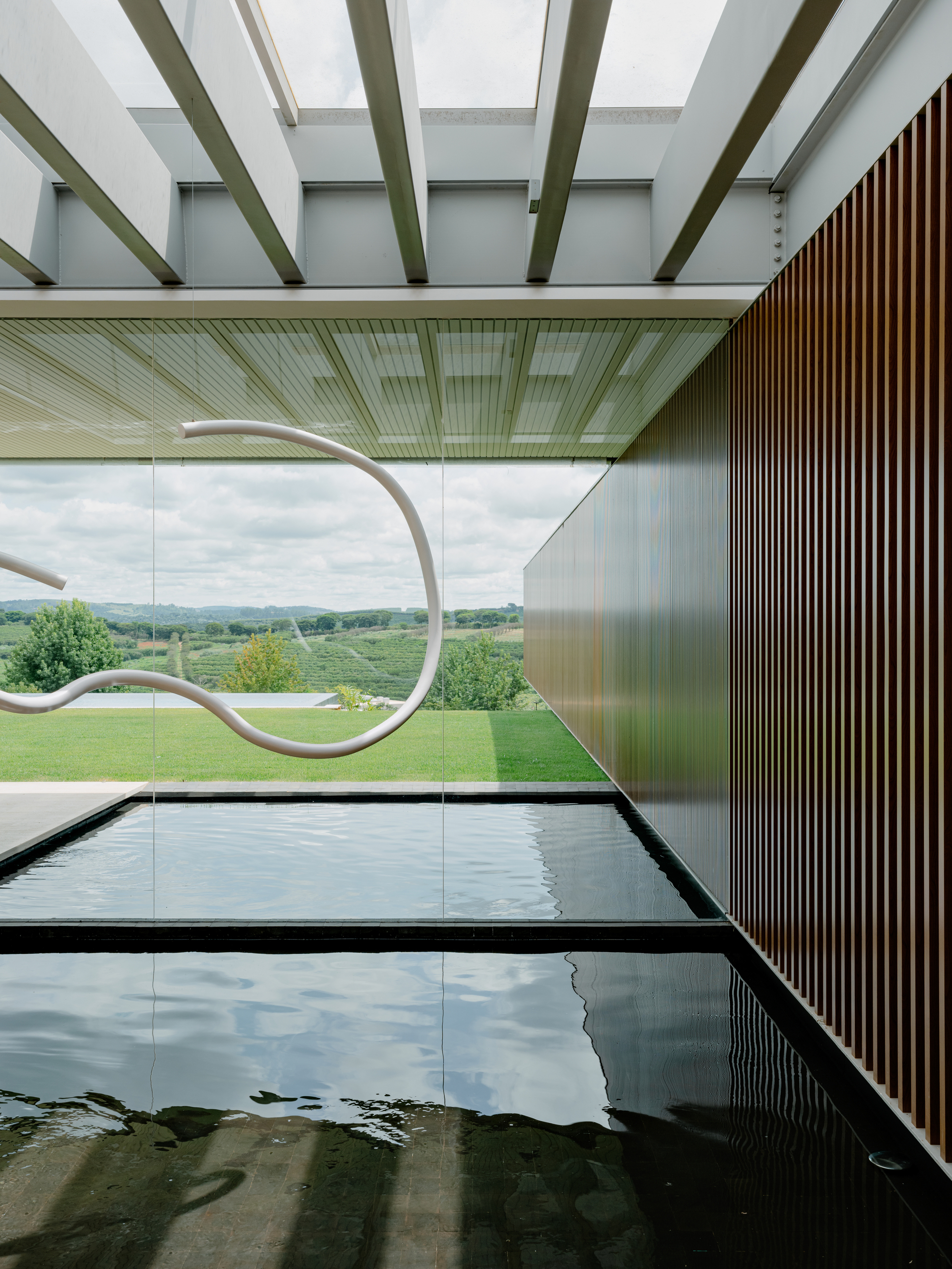View along the indoor pool showing timber slat wall and full-height glazing overlooking the landscape