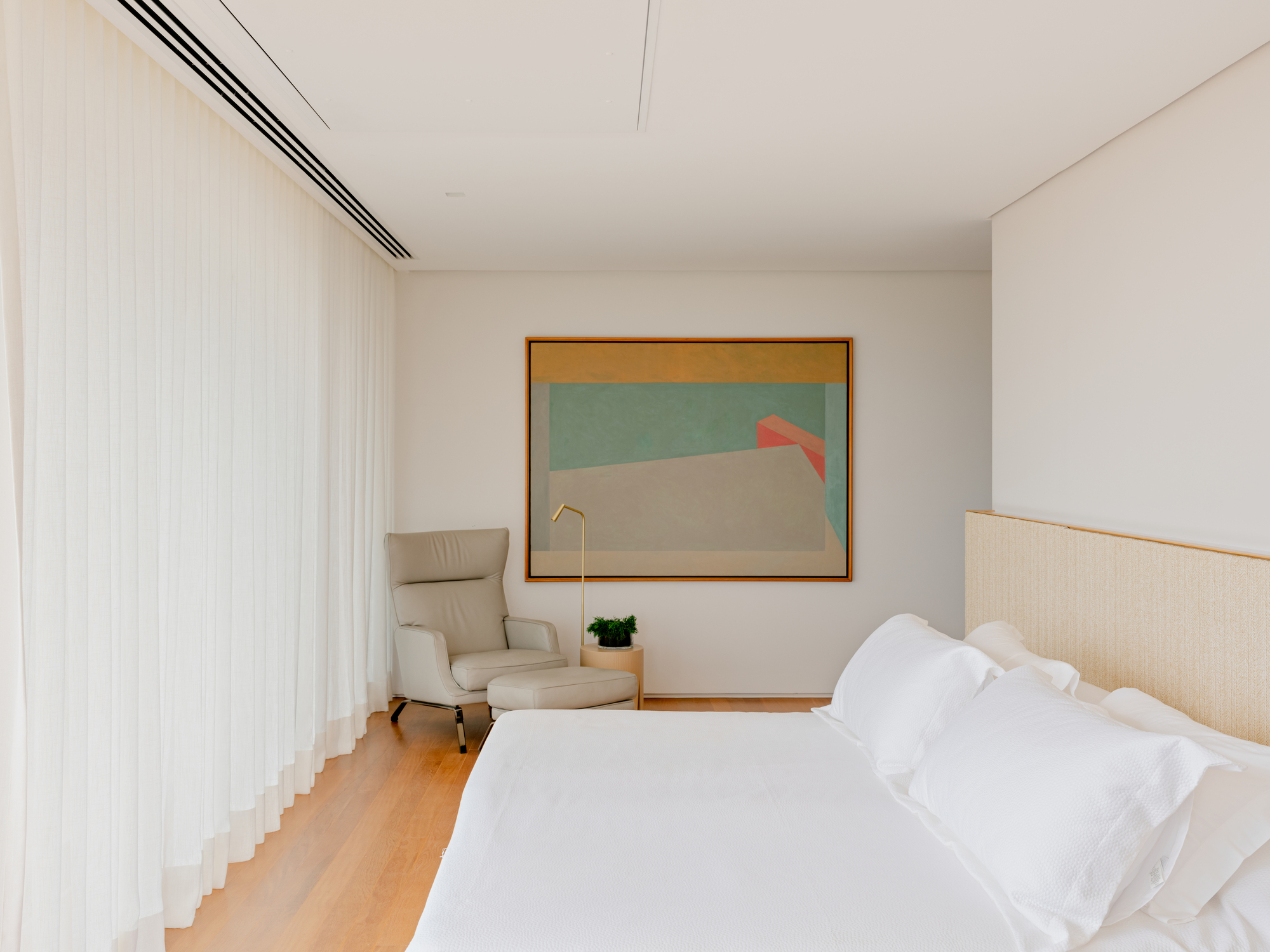 Bedroom corner with upholstered armchair beneath framed artwork and linear ceiling diffuser