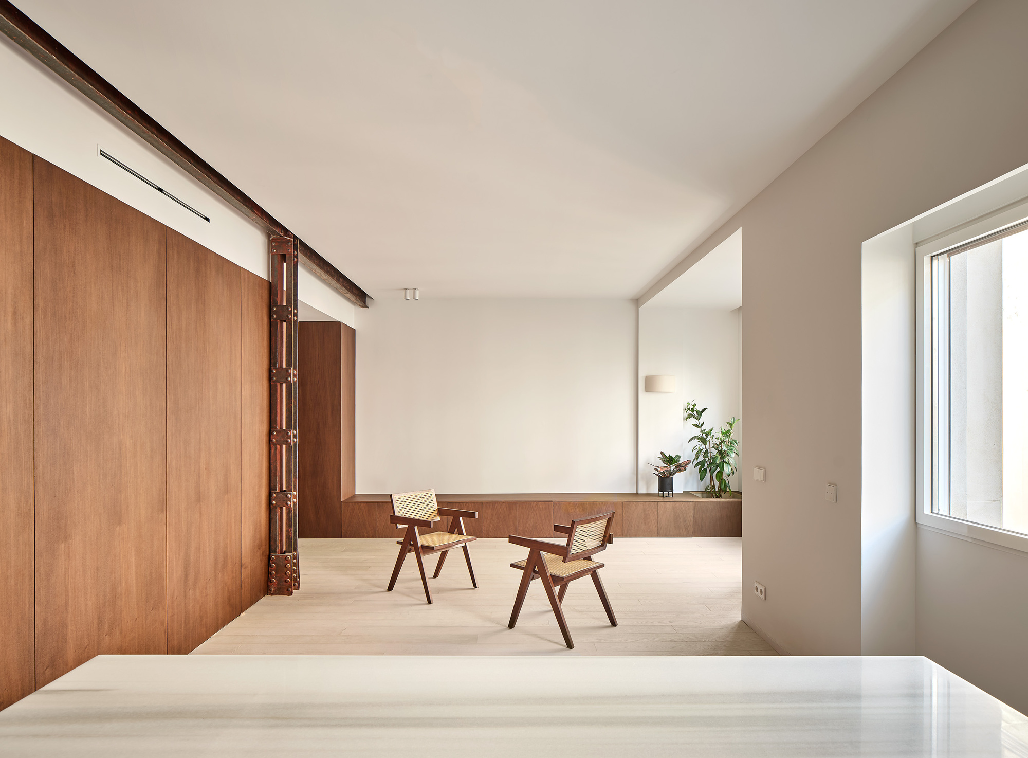 Open space with two wooden chairs beside a low timber bench and potted plants