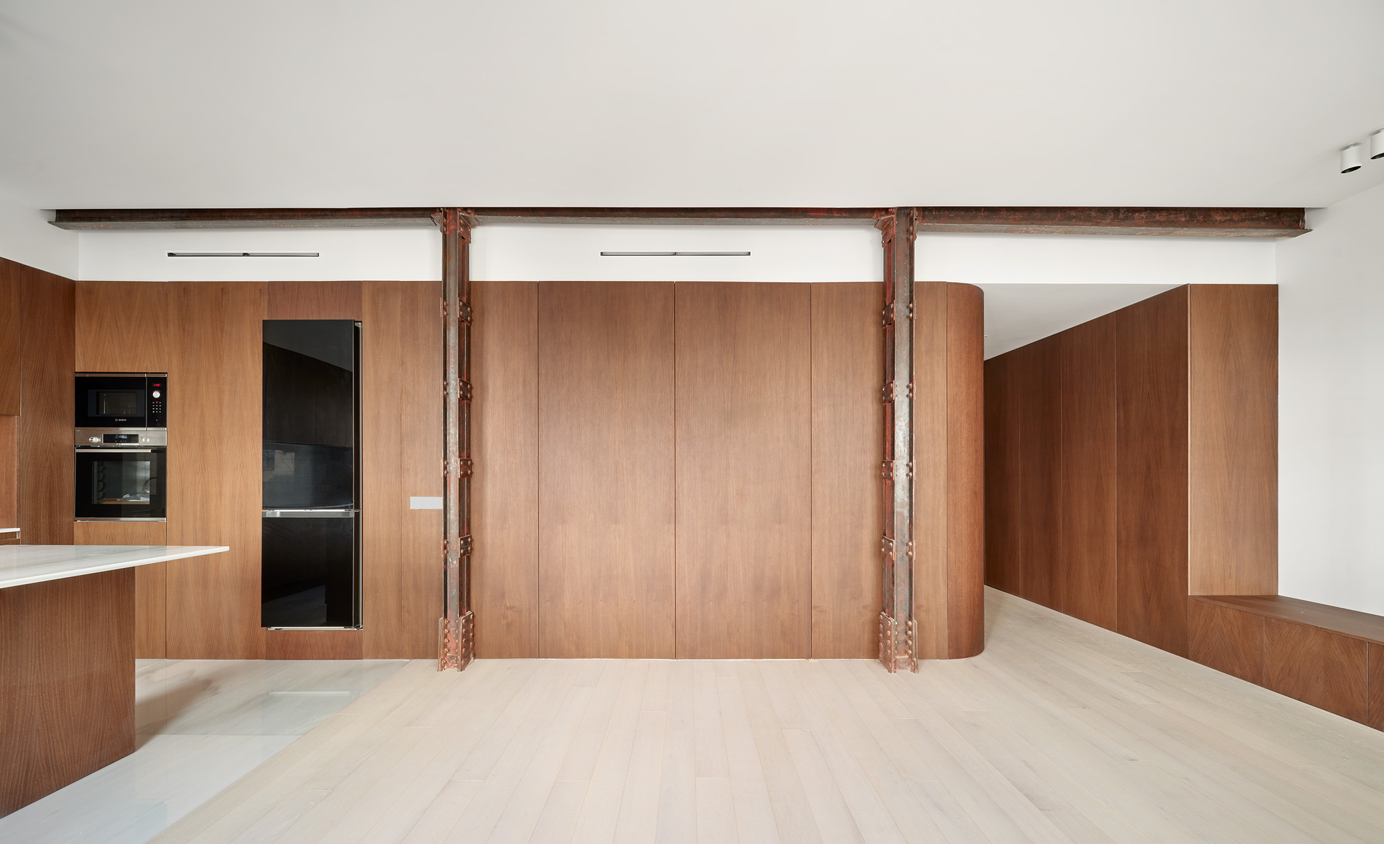 Open living area with exposed steel columns supporting a beam between curved wood storage walls