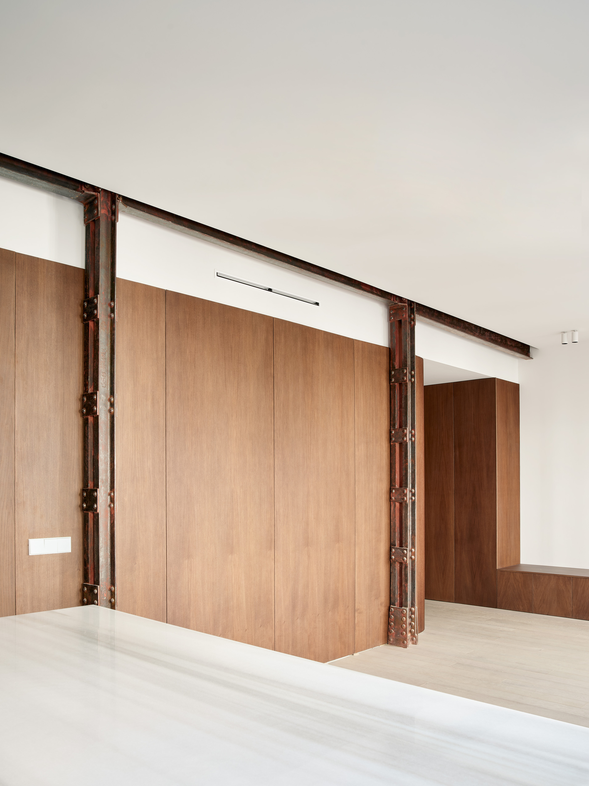 View across white stone countertop toward curved wood wall panels and exposed steel structure
