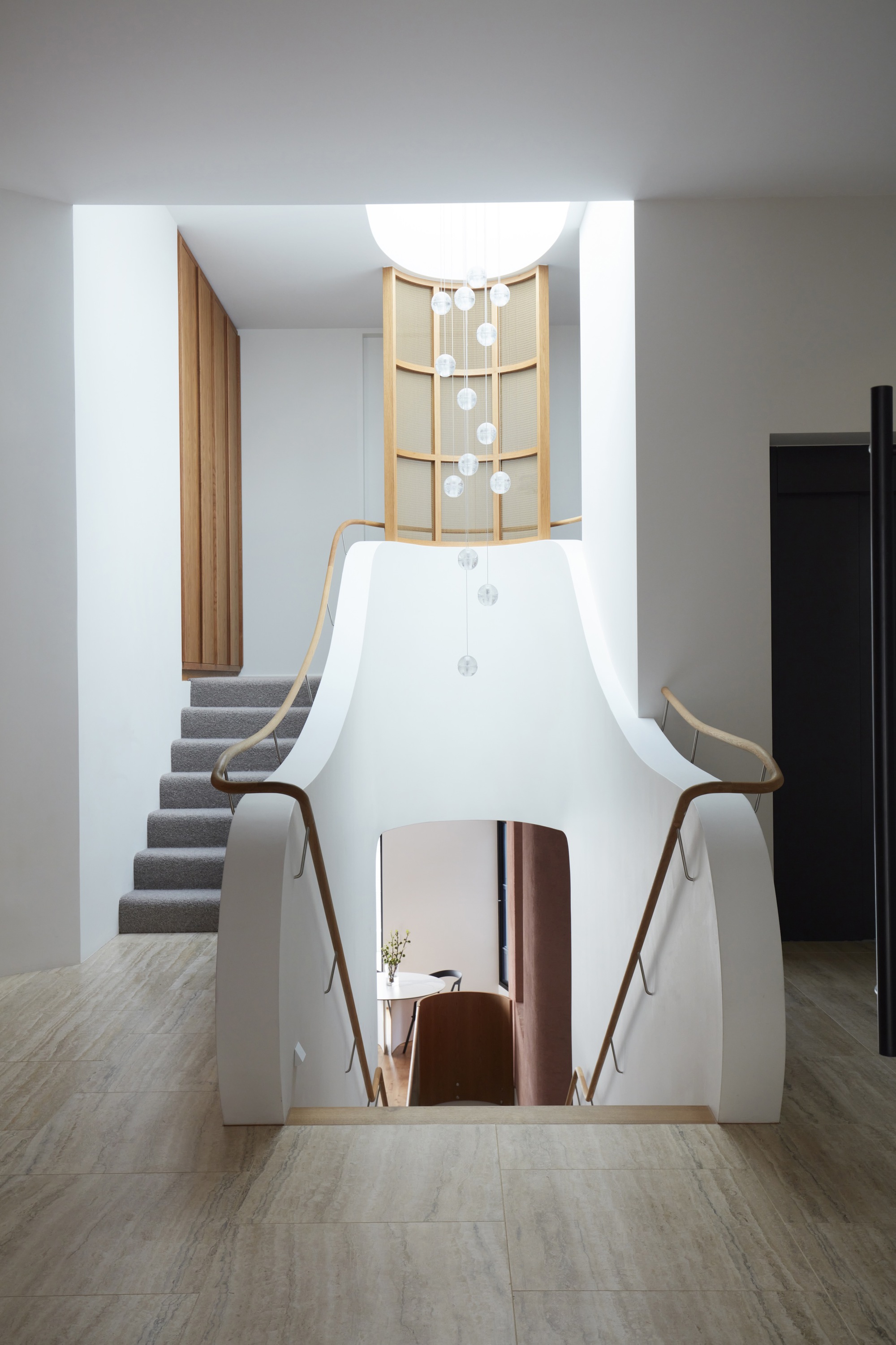 White sculptural stair volume with timber shelving and descending pendant lights under skylight