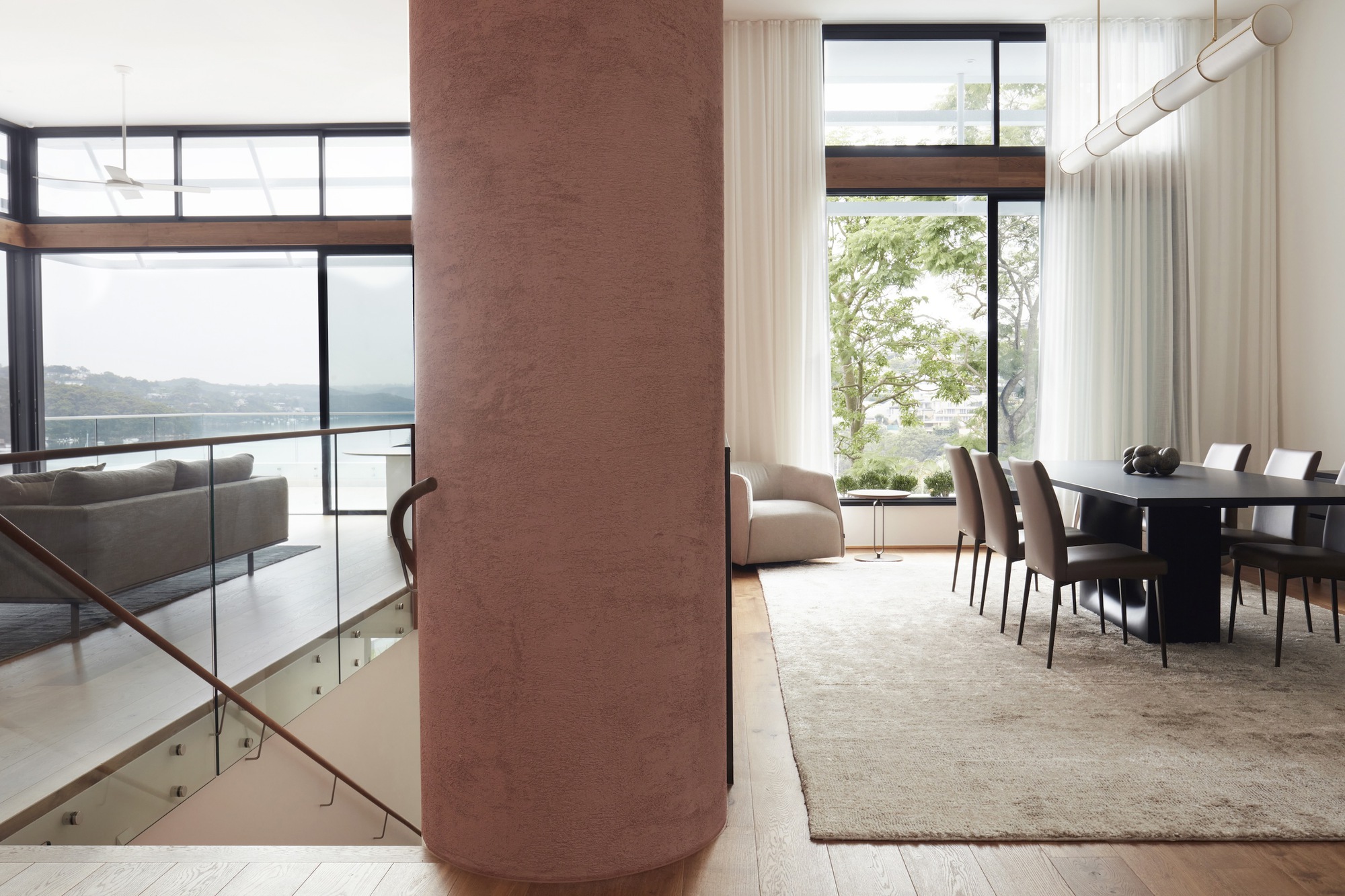 Cylindrical rammed earth column anchoring dining area with harbor views through floor-to-ceiling windows