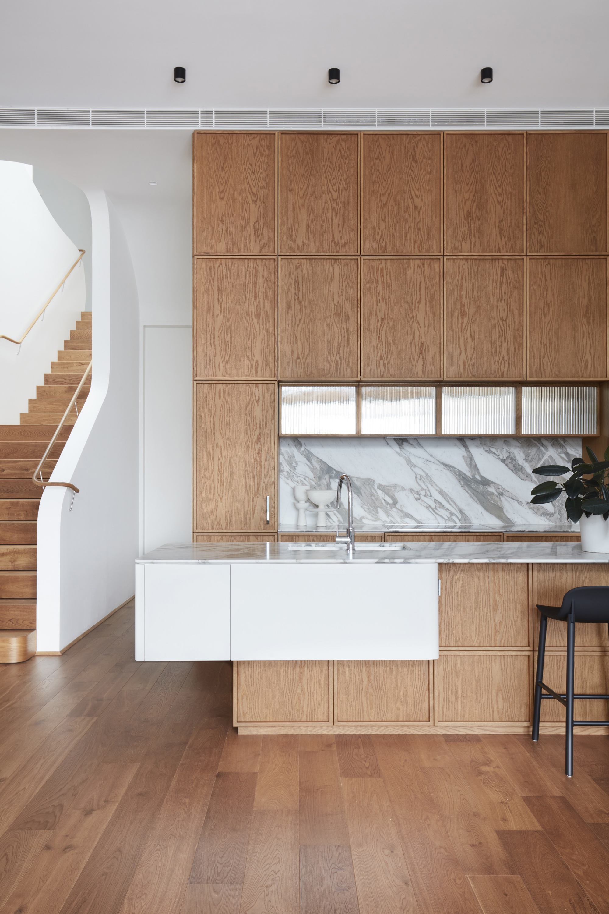 Kitchen with floor-to-ceiling oak veneer cabinetry and marble backsplash beside the timber staircase