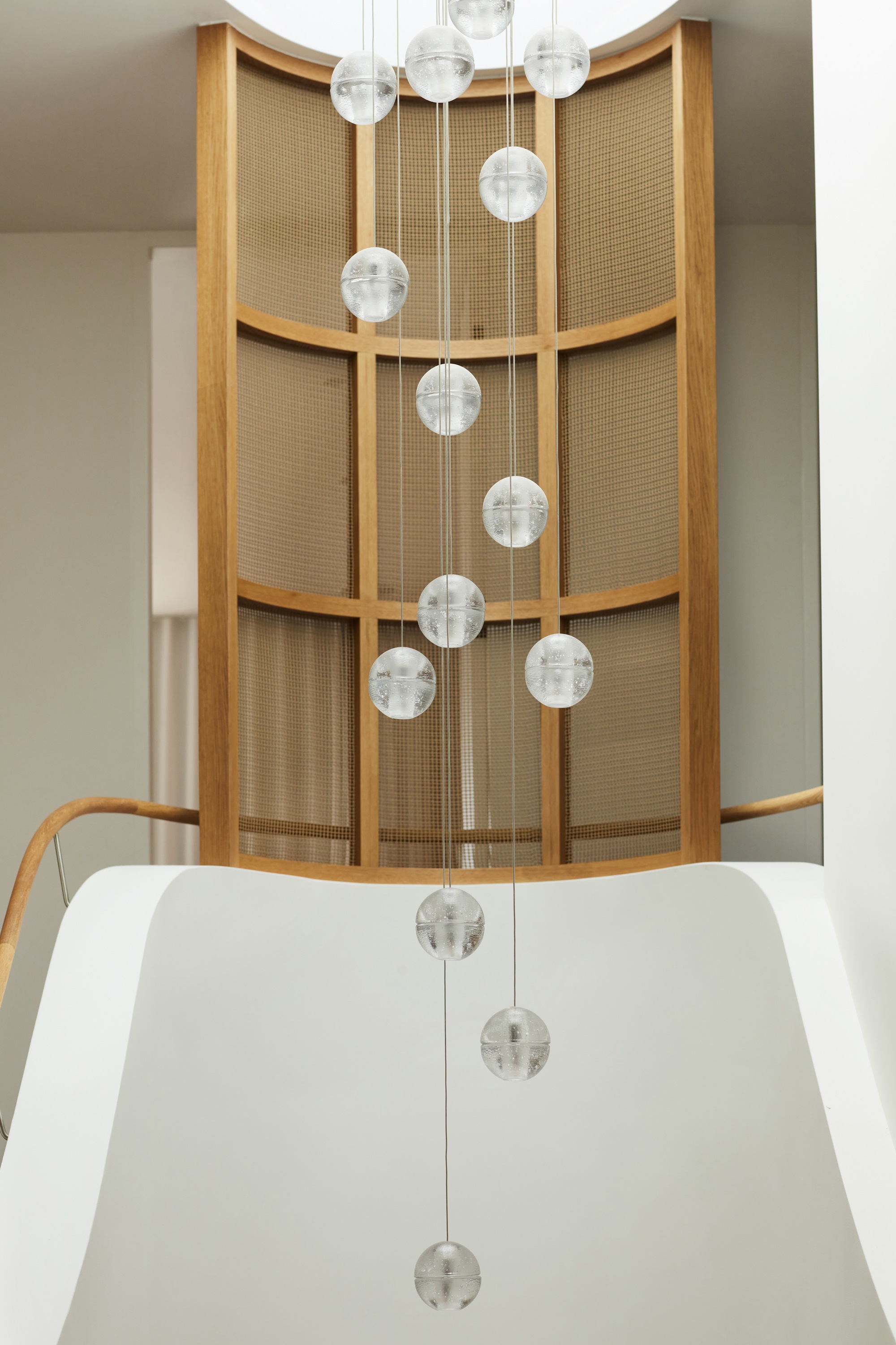 Cascading glass pendant lights in the curved stairwell with oak-framed woven cane screens
