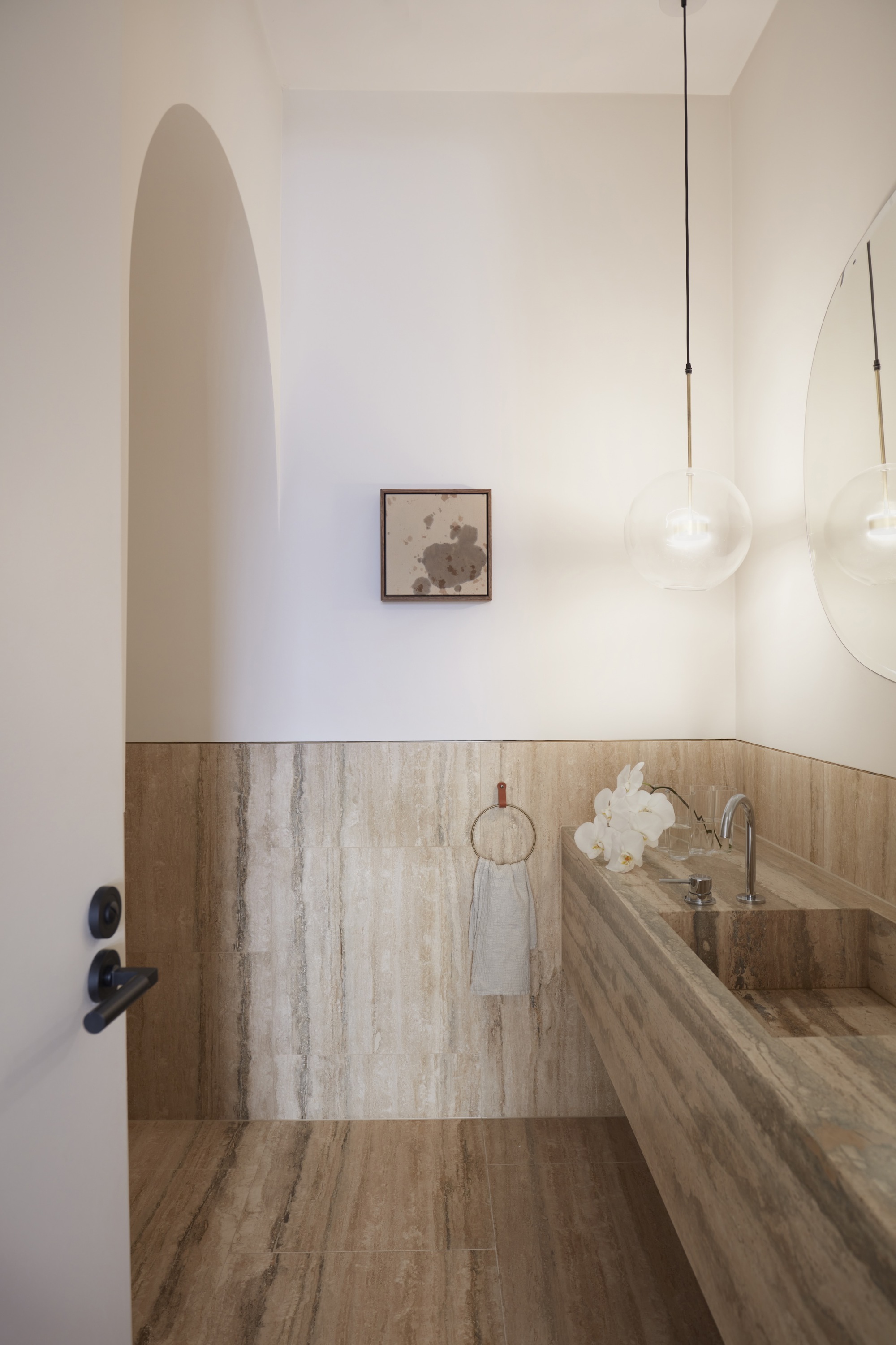 Powder room with travertine wainscoting and an arched doorway with pendant light above
