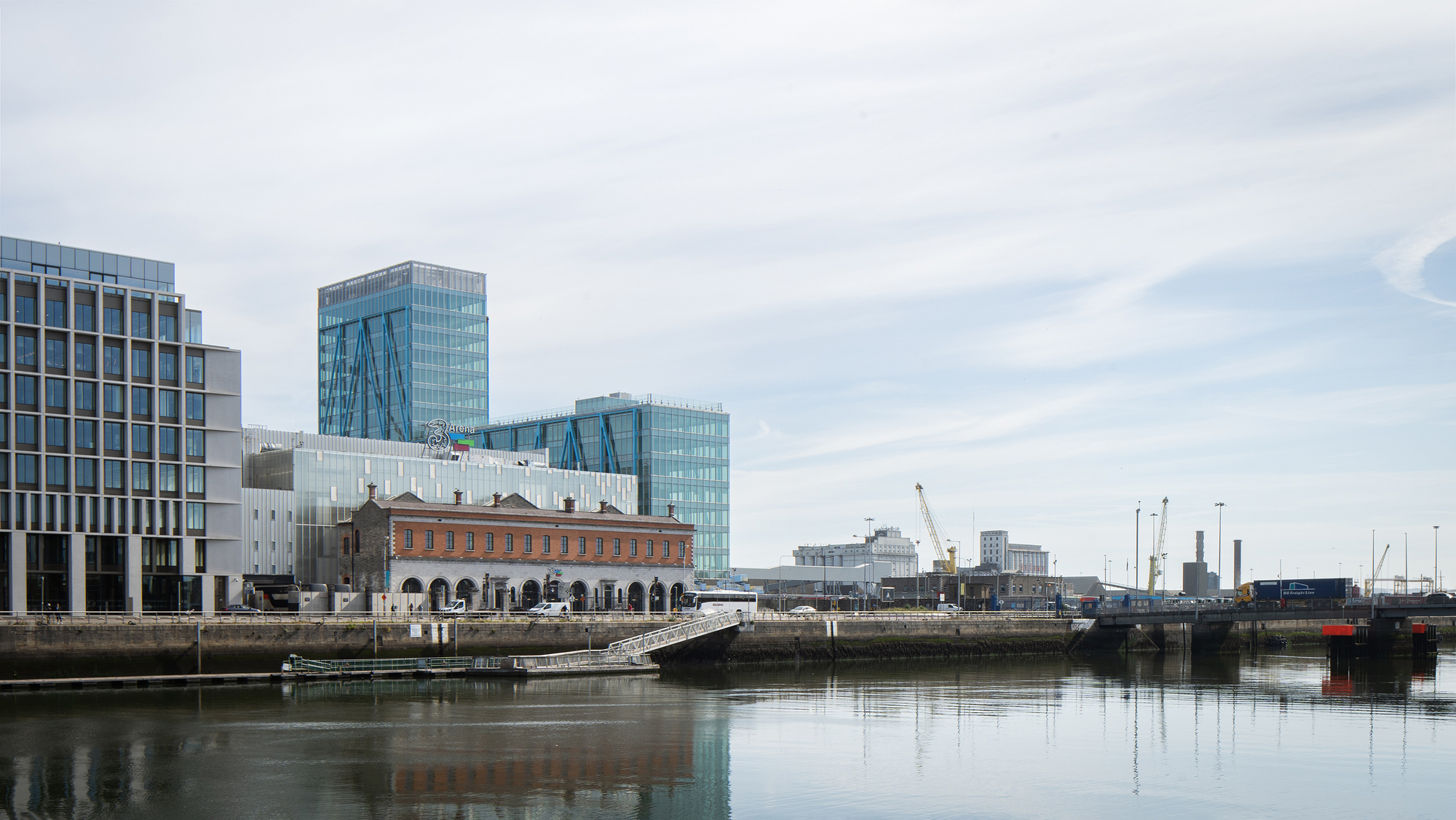 Waterside view of glass towers rising behind a restored brick warehouse with arched openings