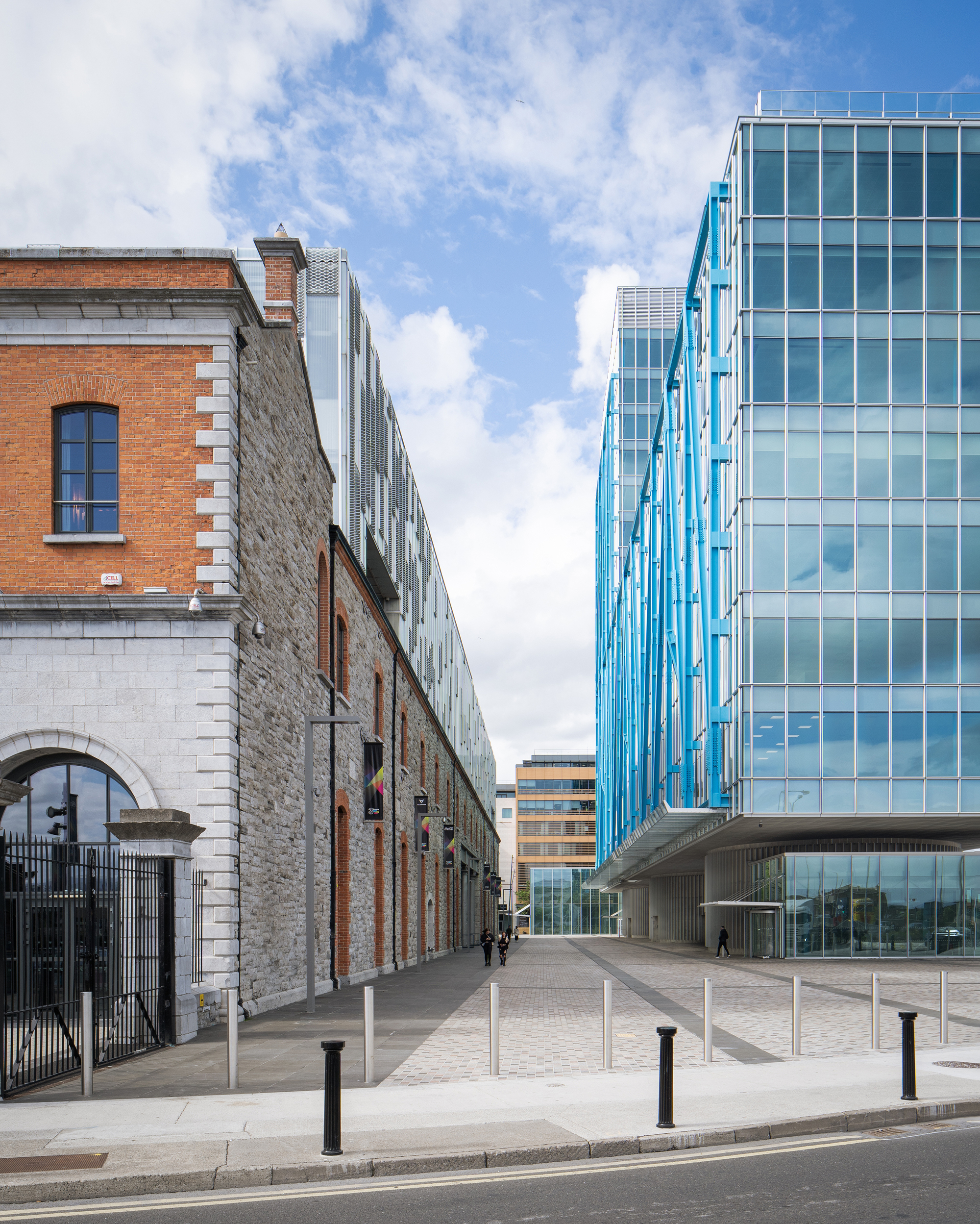 Street view showing stone warehouse facade alongside glass tower with diagonal blue steel exoskeleton