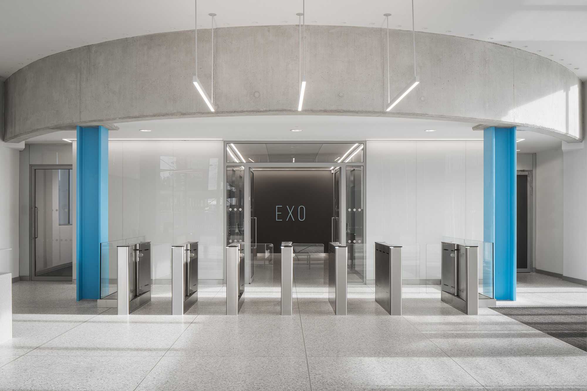 Security turnstile bank beneath a curved concrete soffit with blue columns flanking the entrance corridor