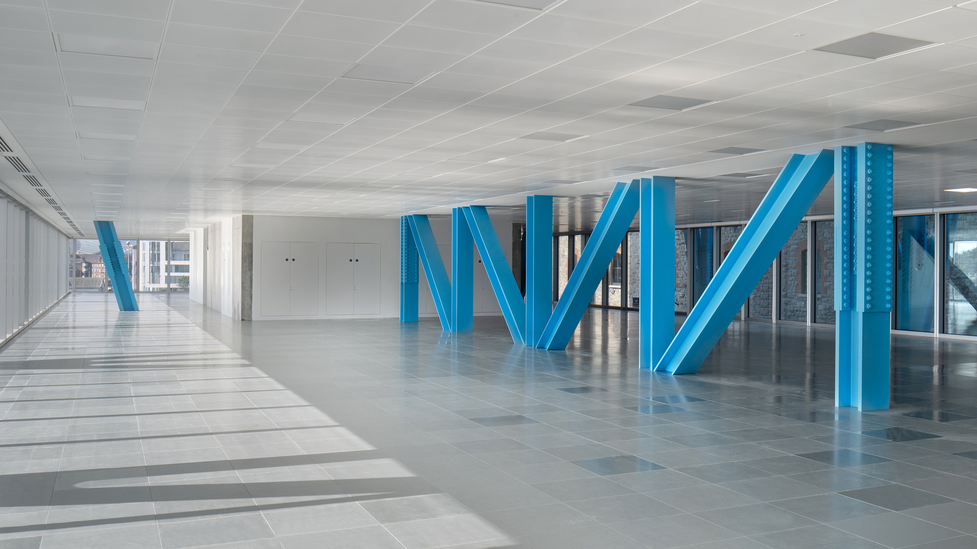 Interior lobby with diagonal blue steel columns supporting a white coffered ceiling above polished tile floors
