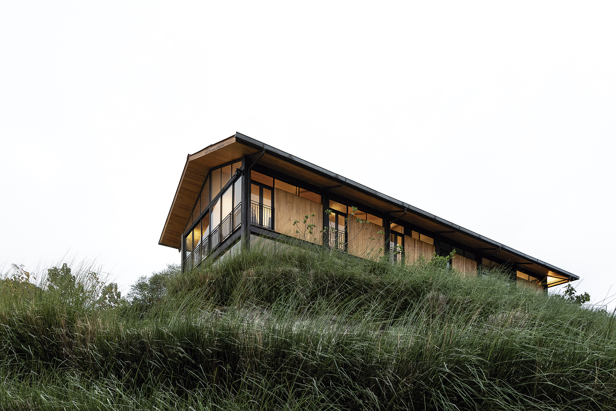 Side elevation showing the timber and glass facade partially embedded in native dune grasses