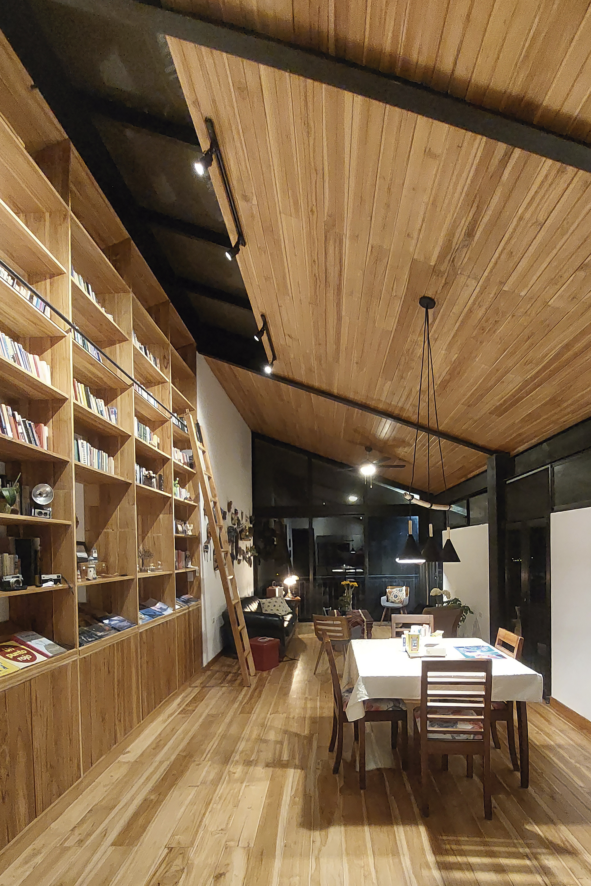 Dining area with timber bookshelf wall and slat ceiling under exposed black steel beams