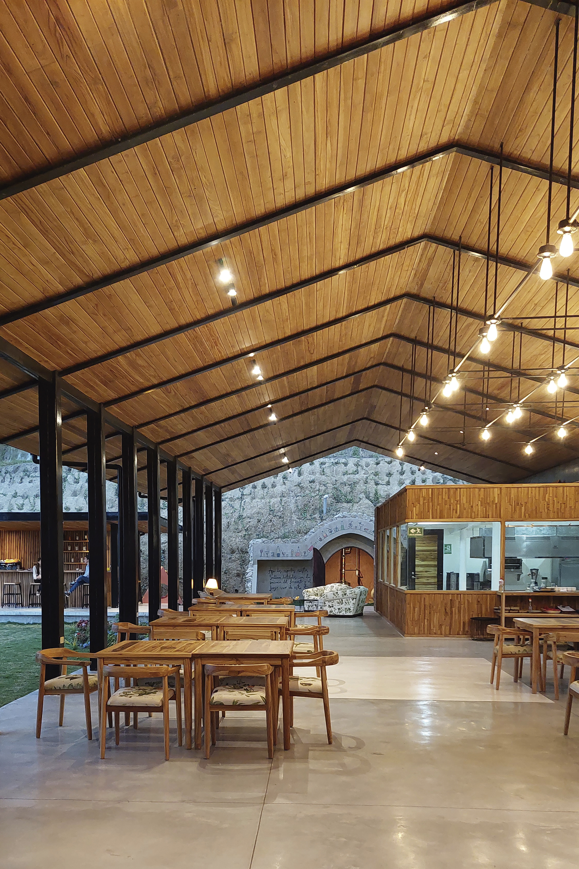 Dining hall with gabled timber ceiling, steel columns and string lights above timber tables
