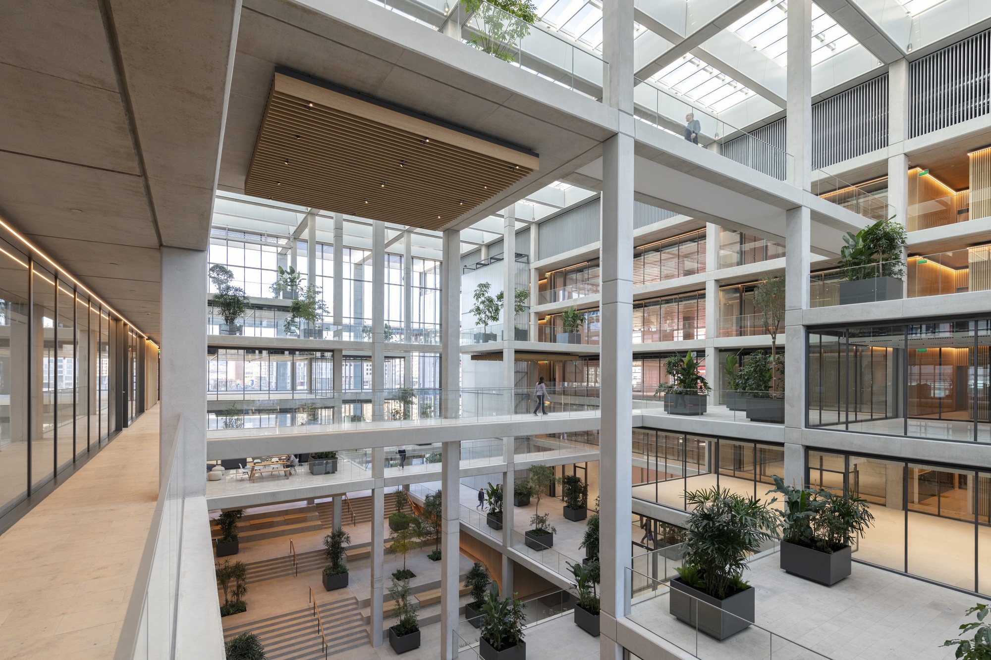 Atrium corridor view showing suspended timber ceiling panels and potted trees on multiple levels