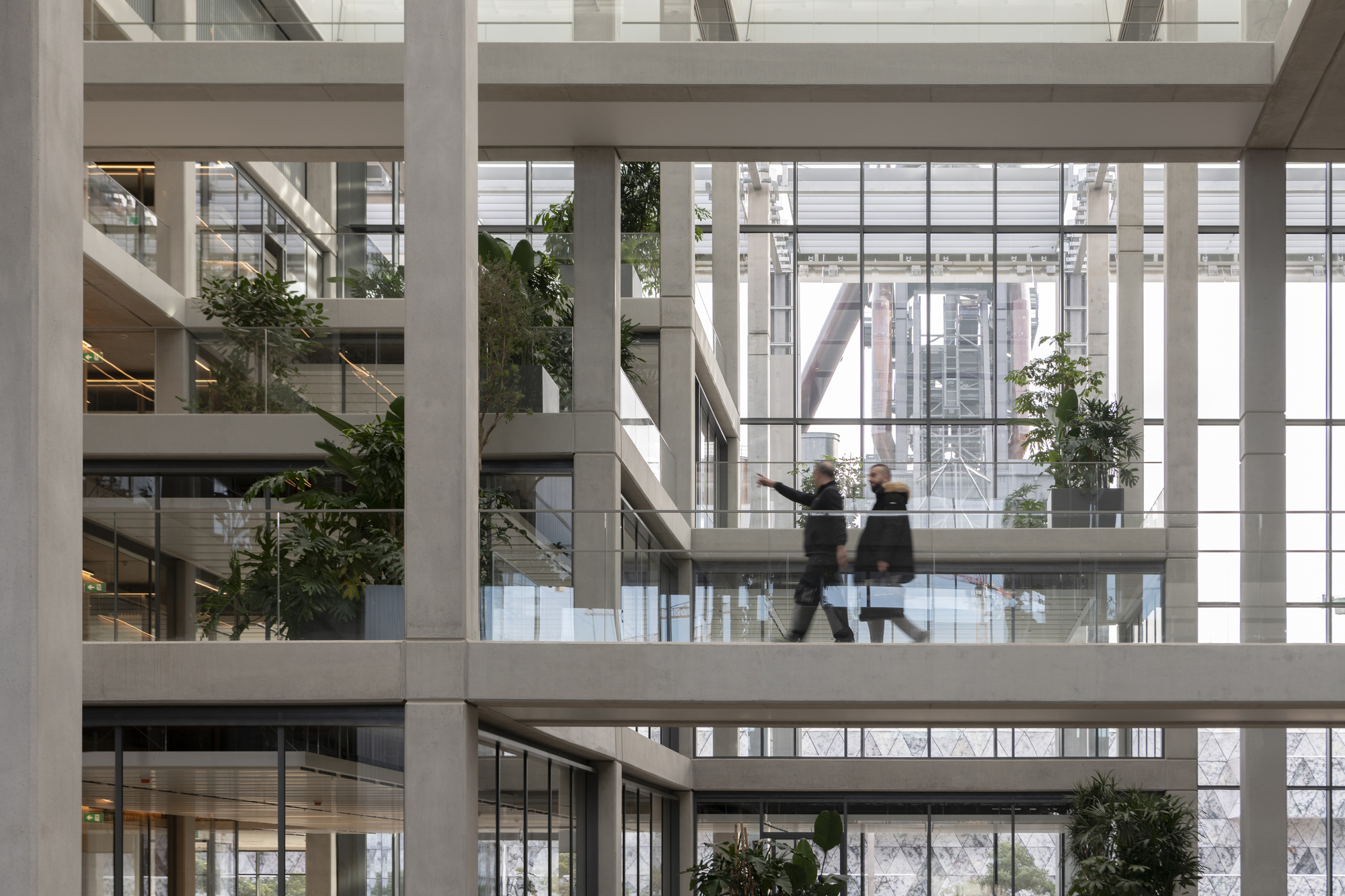 Atrium walkway with two figures in motion and greenery on tiered levels
