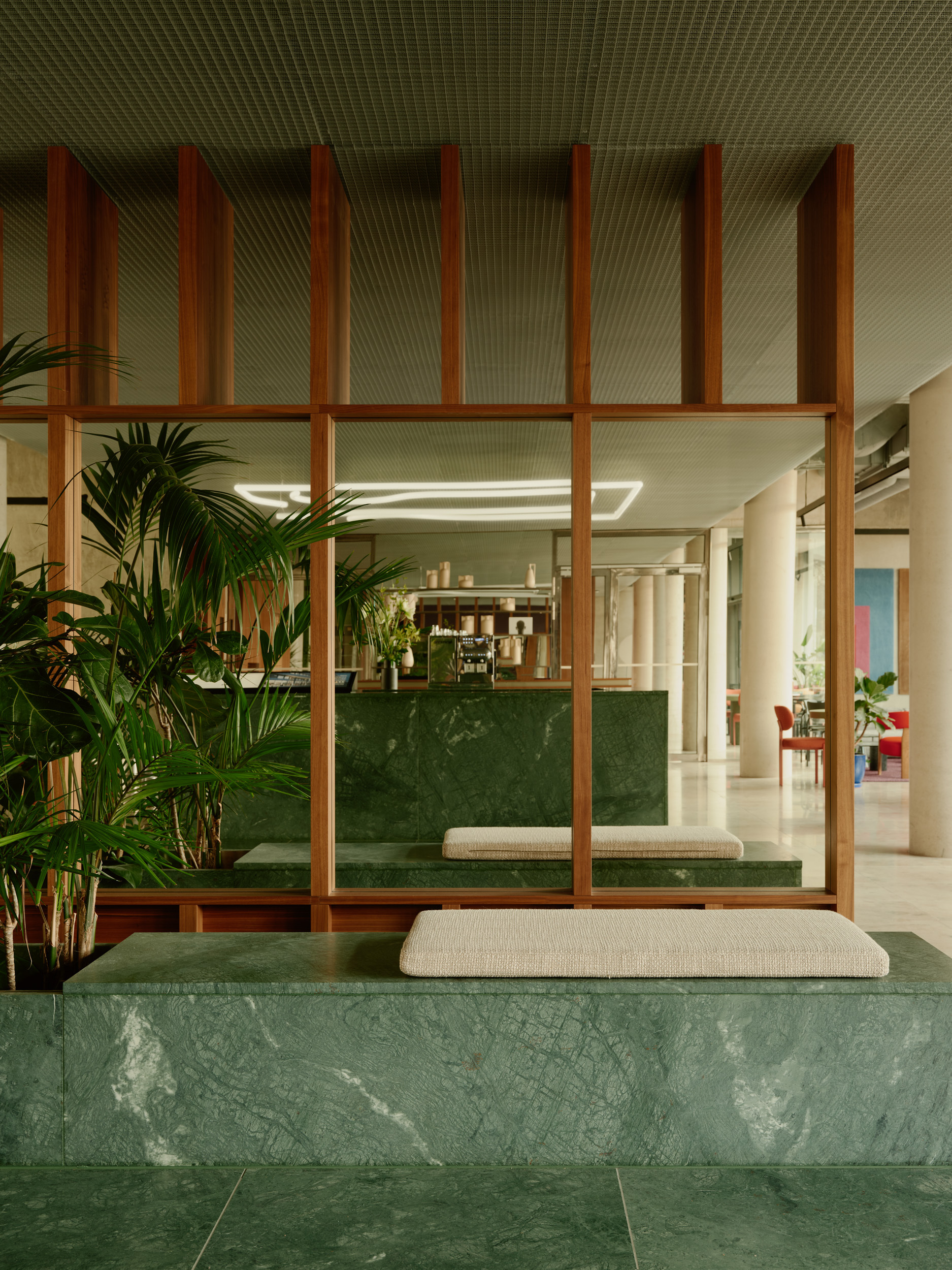 Green marble bench with cushion seating below a timber screen partition and planted palms