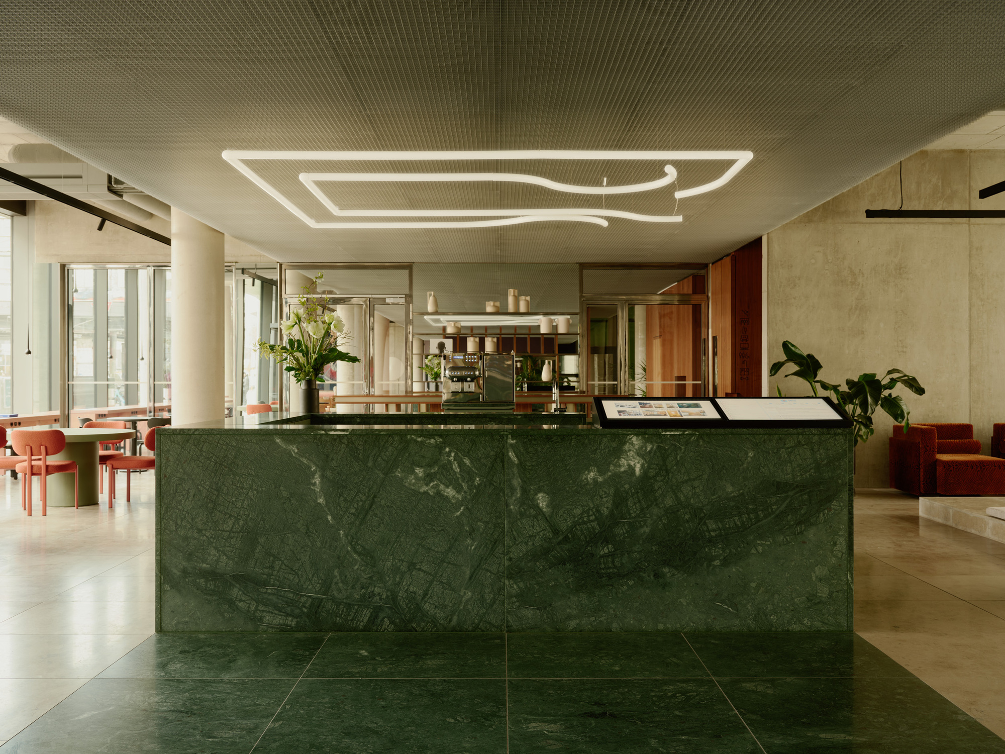 Reception desk clad in green marble slabs beneath a slatted ceiling and linear light fixture