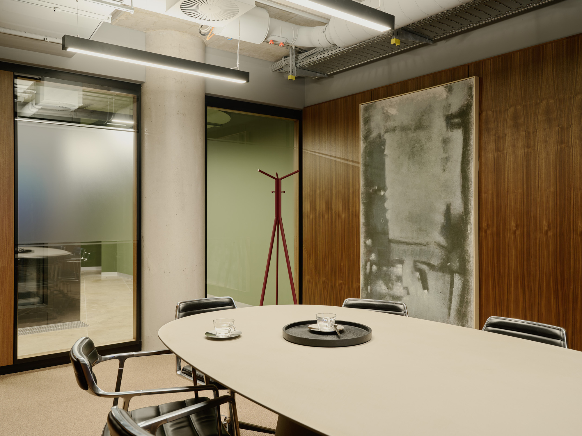 Meeting room with oval table and exposed concrete ceiling ducts beside wood paneling and artwork