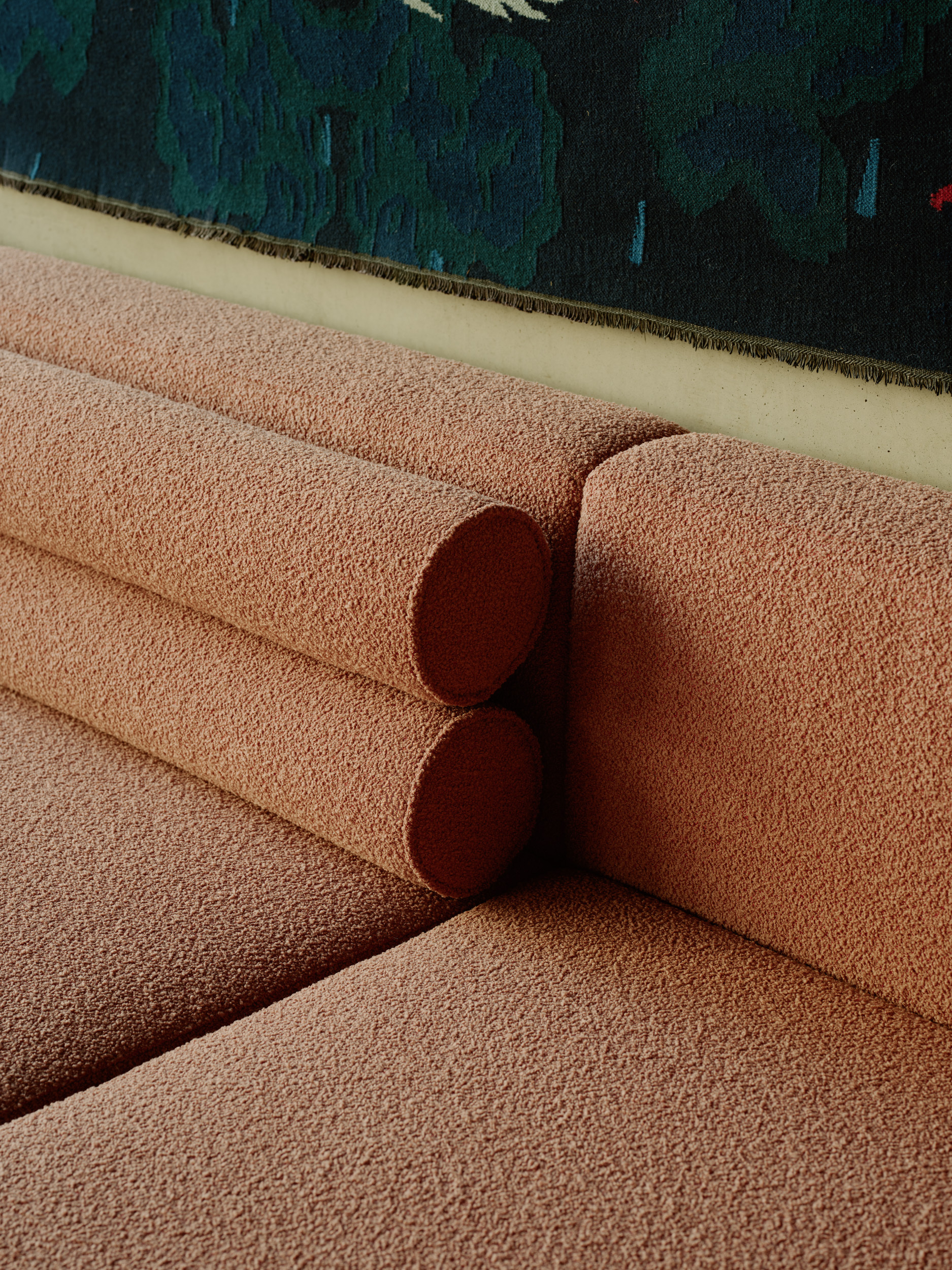 Close-up of a pink textured sofa with cylindrical cushion against a deep blue tapestry