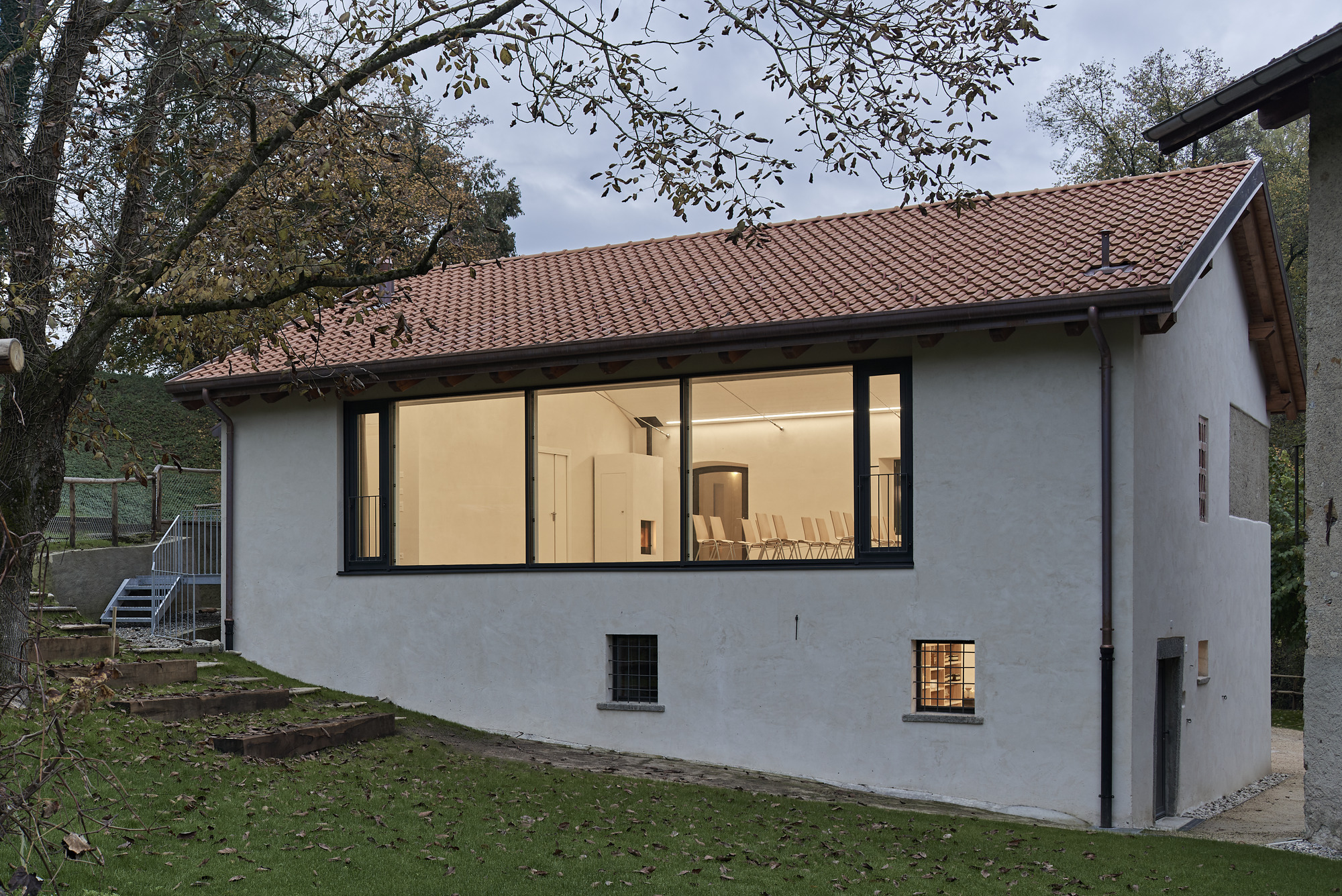 Garden view of the white rendered facade with large picture window and red clay tile roof under overhanging branches