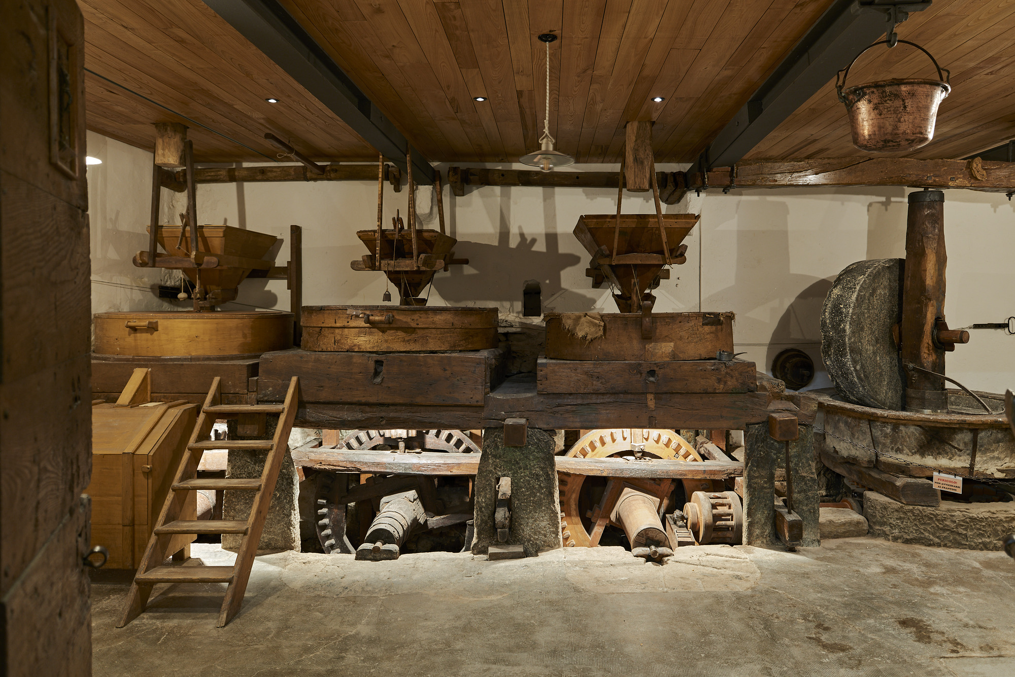 Historic mill machinery with wooden hoppers, stone wheels and timber beams under a plank ceiling