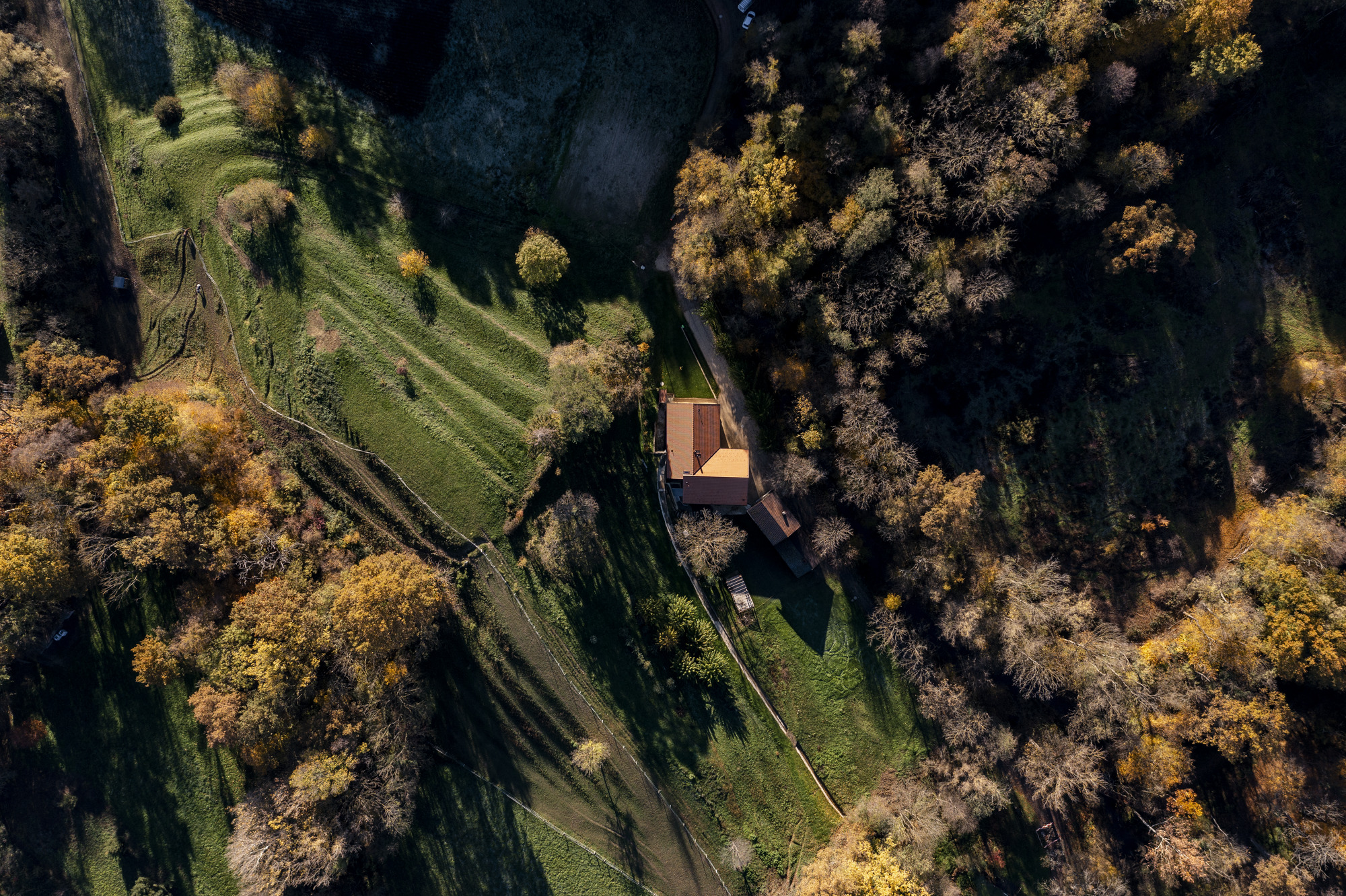 Aerial view of the tiled roof compound nestled between meadows and autumn woodland with long shadows