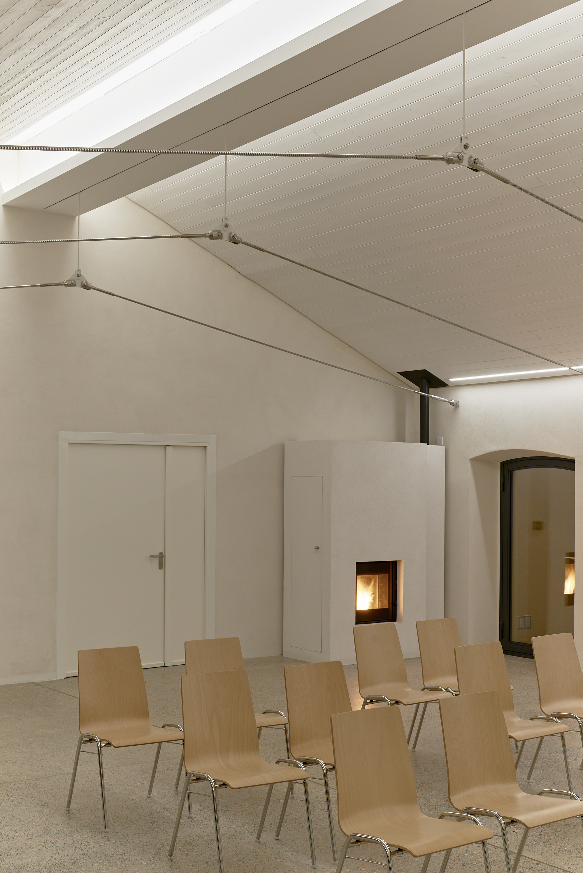 Vaulted ceiling with tensioned fabric panels and cable supports above rows of plywood chairs and fireplace insert