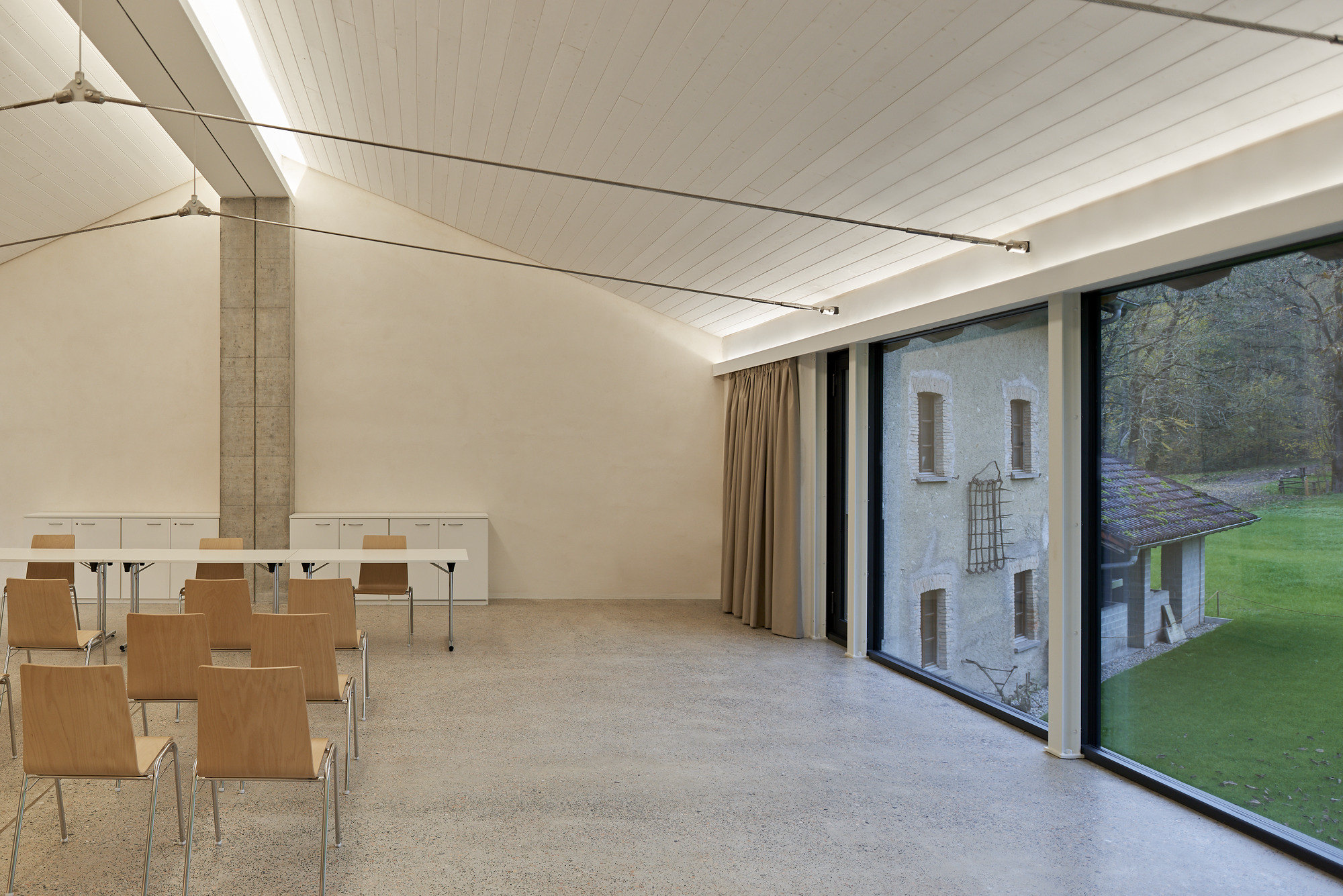 Meeting room with floor-to-ceiling glazing framing view of hillside and weathered stone building beyond