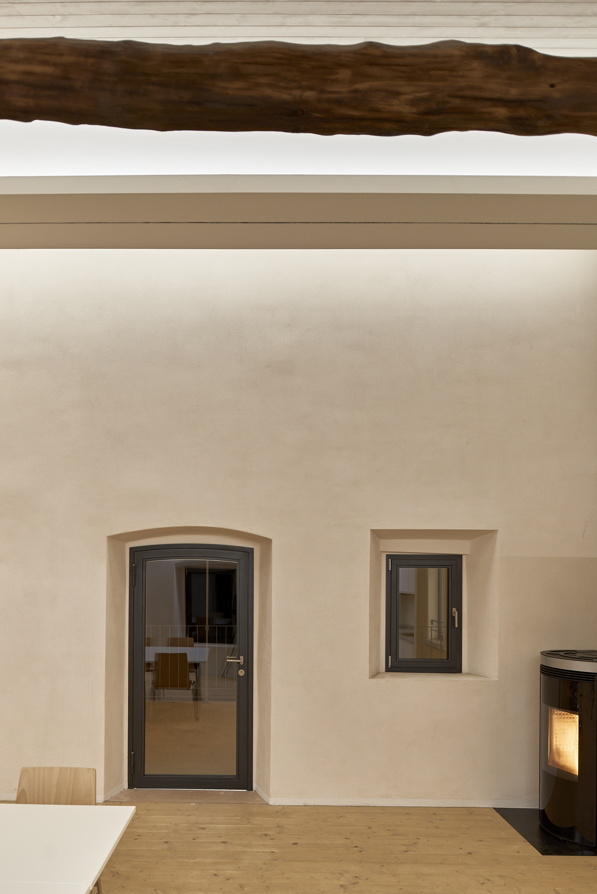 Interior wall with arched doorway, square window opening, exposed timber beam overhead, and pellet stove