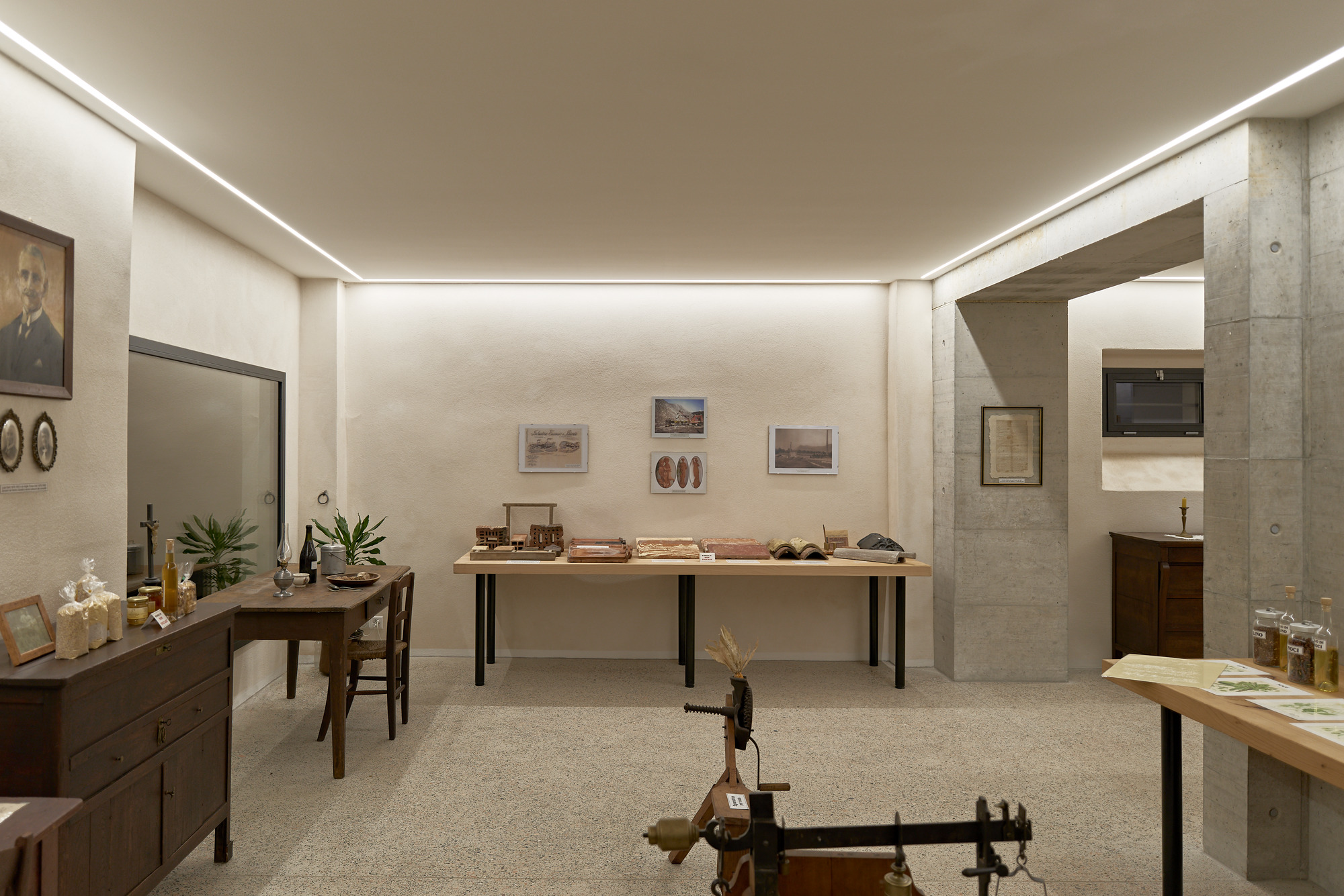 Exhibition room with exposed concrete columns and perimeter cove lighting illuminating display tables