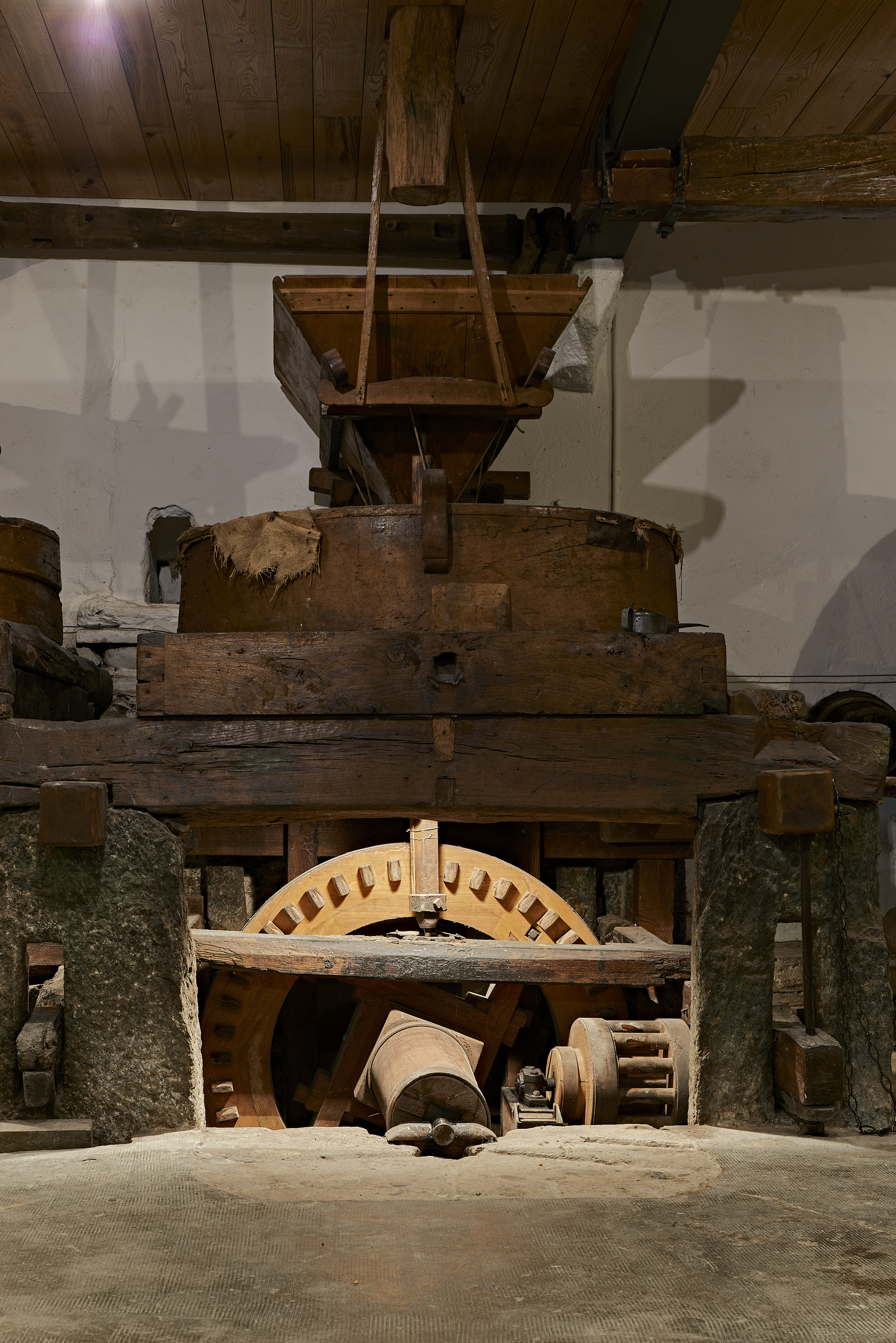 Historic wooden mill machinery with timber gears and hopper beneath exposed ceiling joists