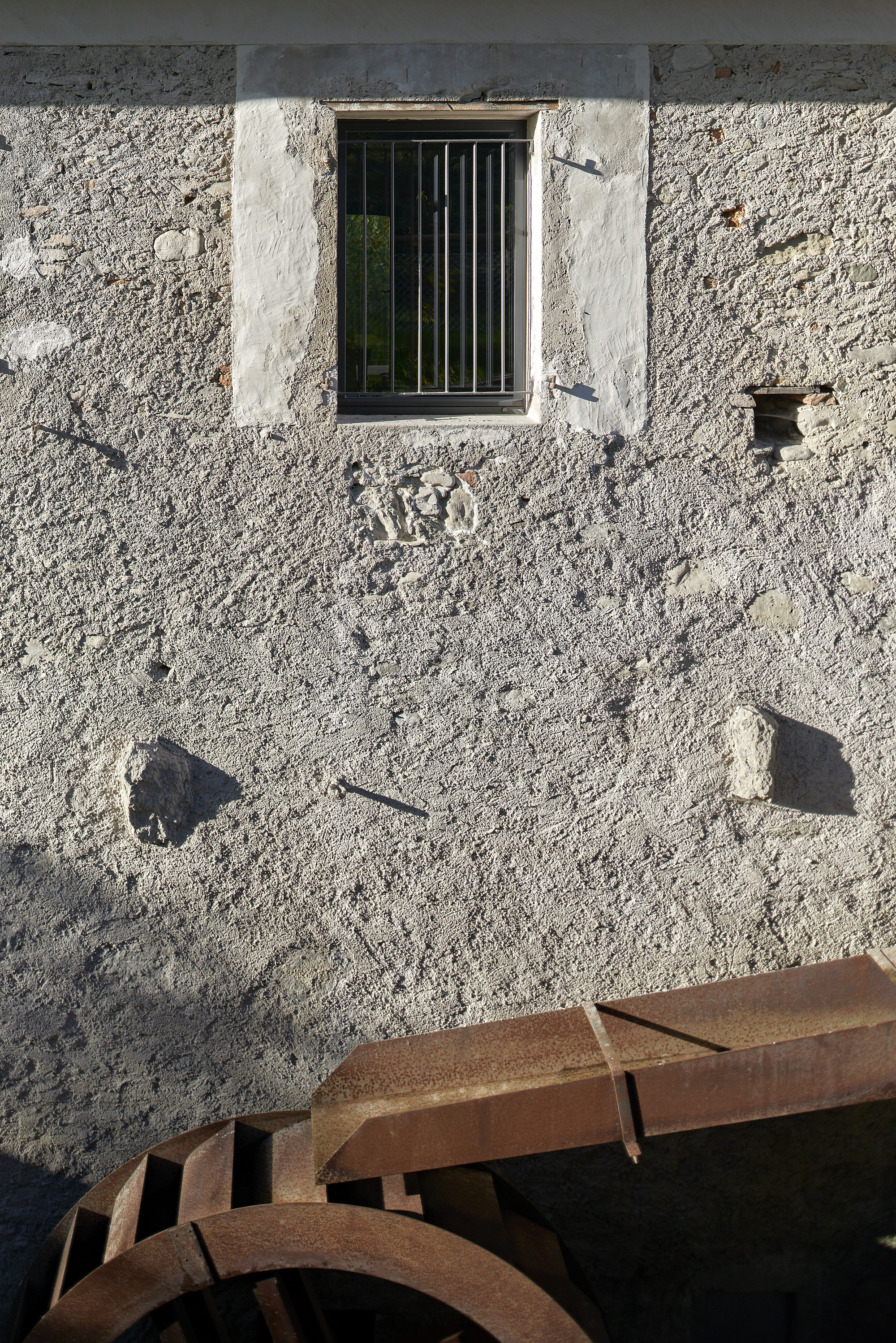 Barred window in weathered stucco facade with rusted ironwork casting afternoon shadows