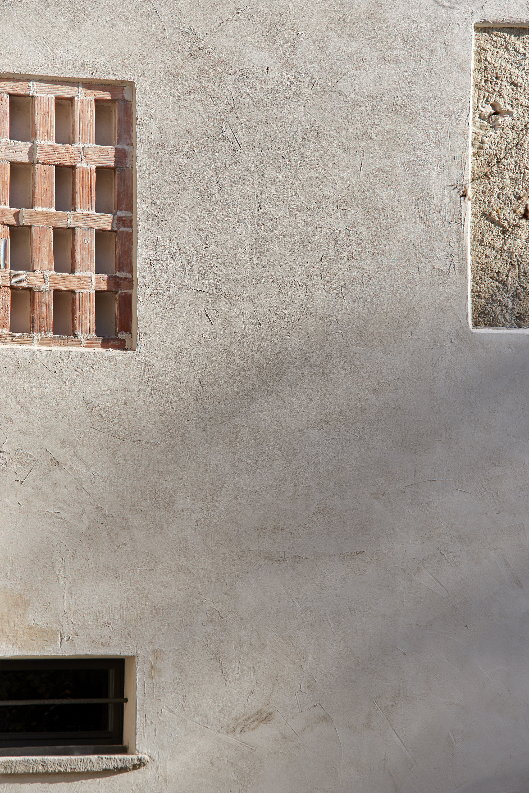 Textured plaster wall with terracotta brick screen window and narrow concrete slit opening