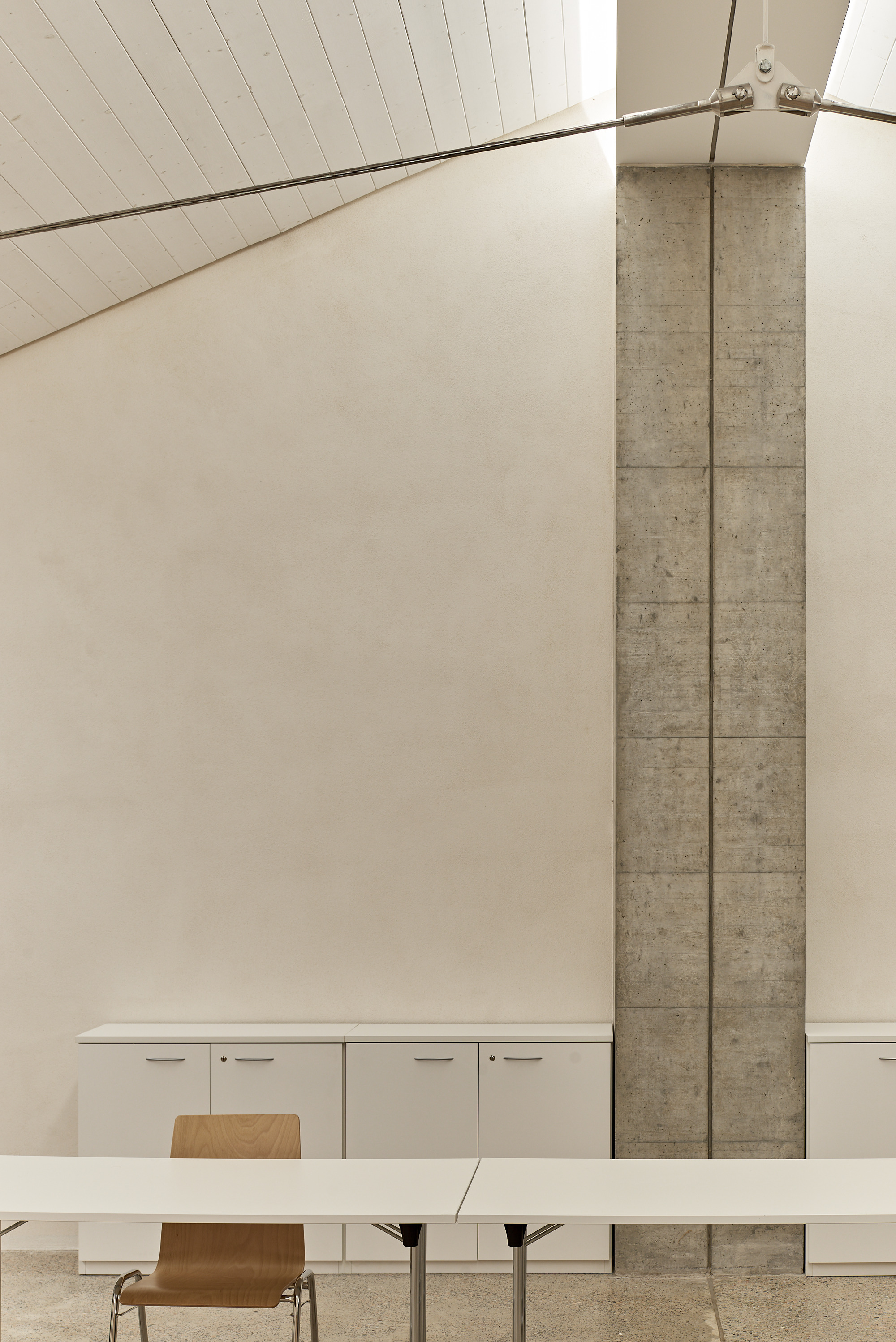 Dining area with exposed concrete column beside white cabinets under a timber slat ceiling