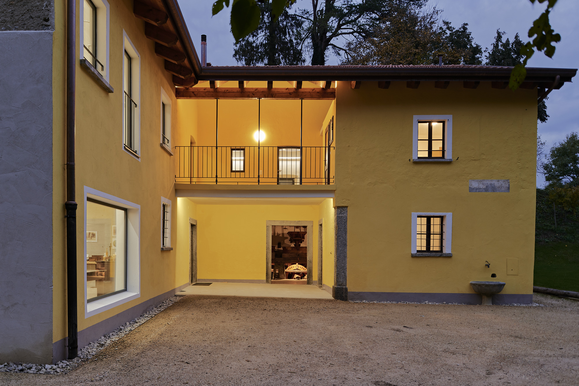 Courtyard view showing ochre volumes with illuminated openings and gravel surface at twilight