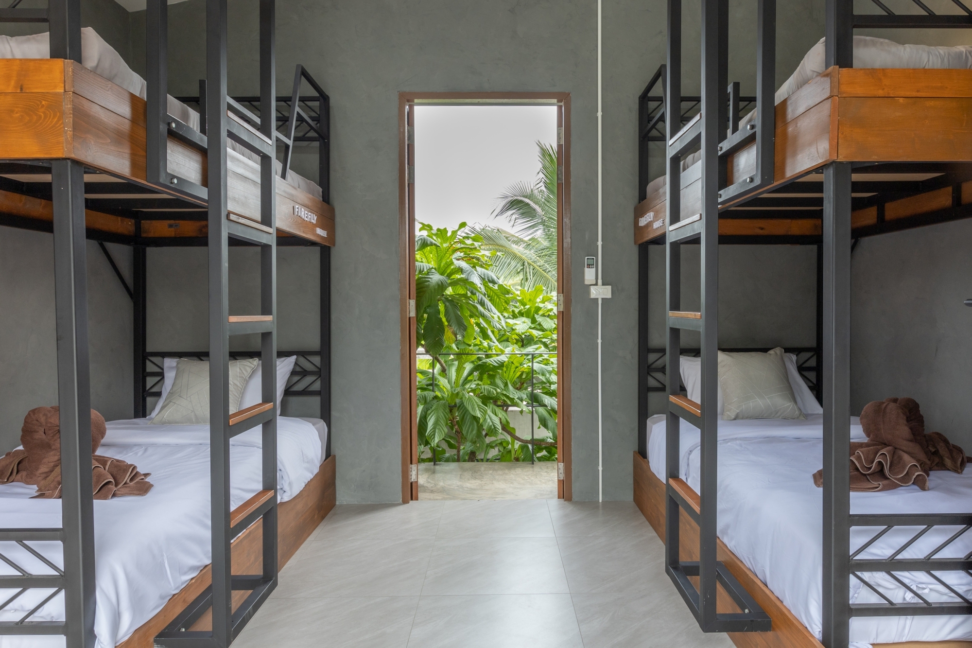 Dormitory room with timber and steel bunk beds flanking a doorway to a planted courtyard