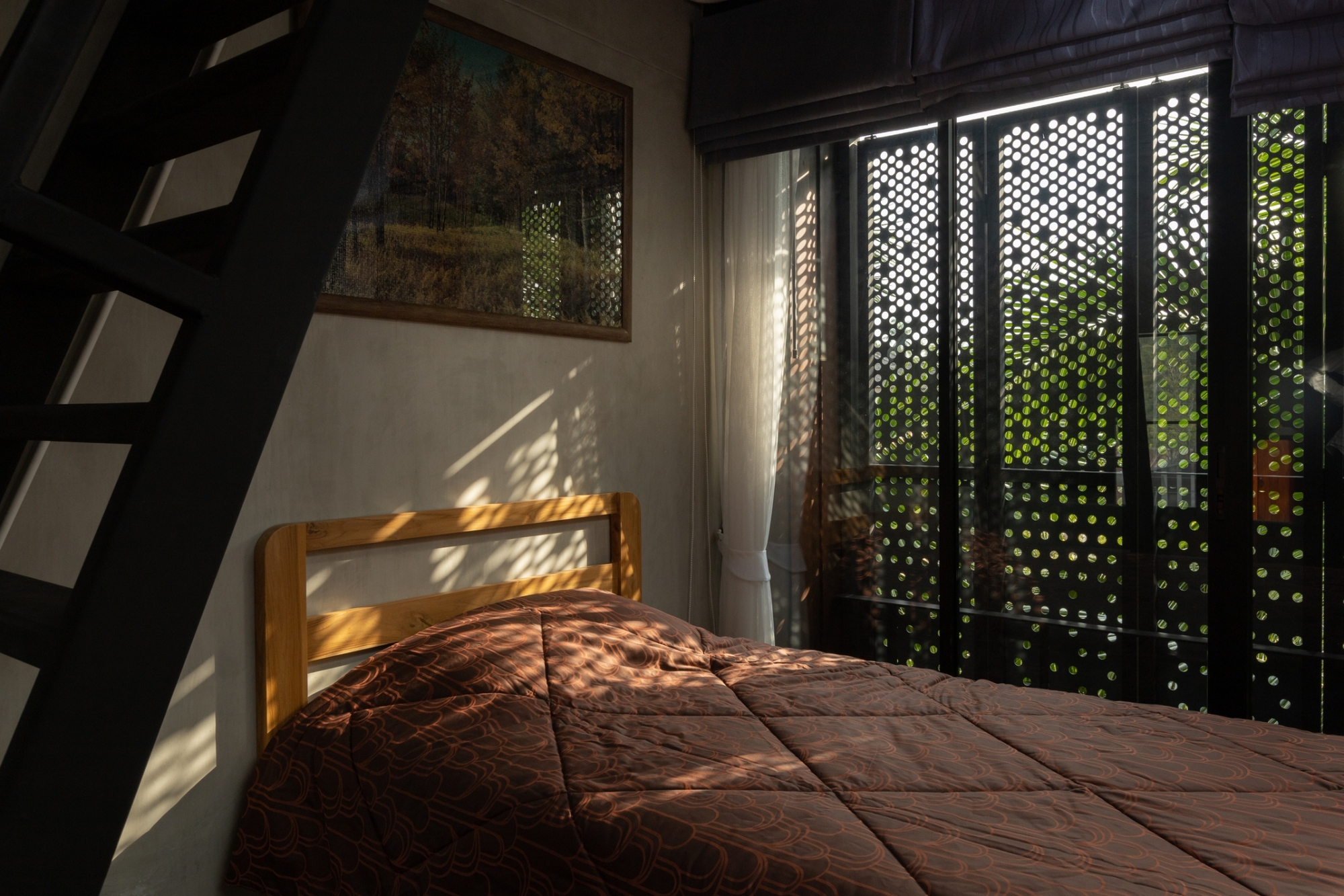 Bedroom with perforated black screens filtering morning sunlight onto a timber bed frame