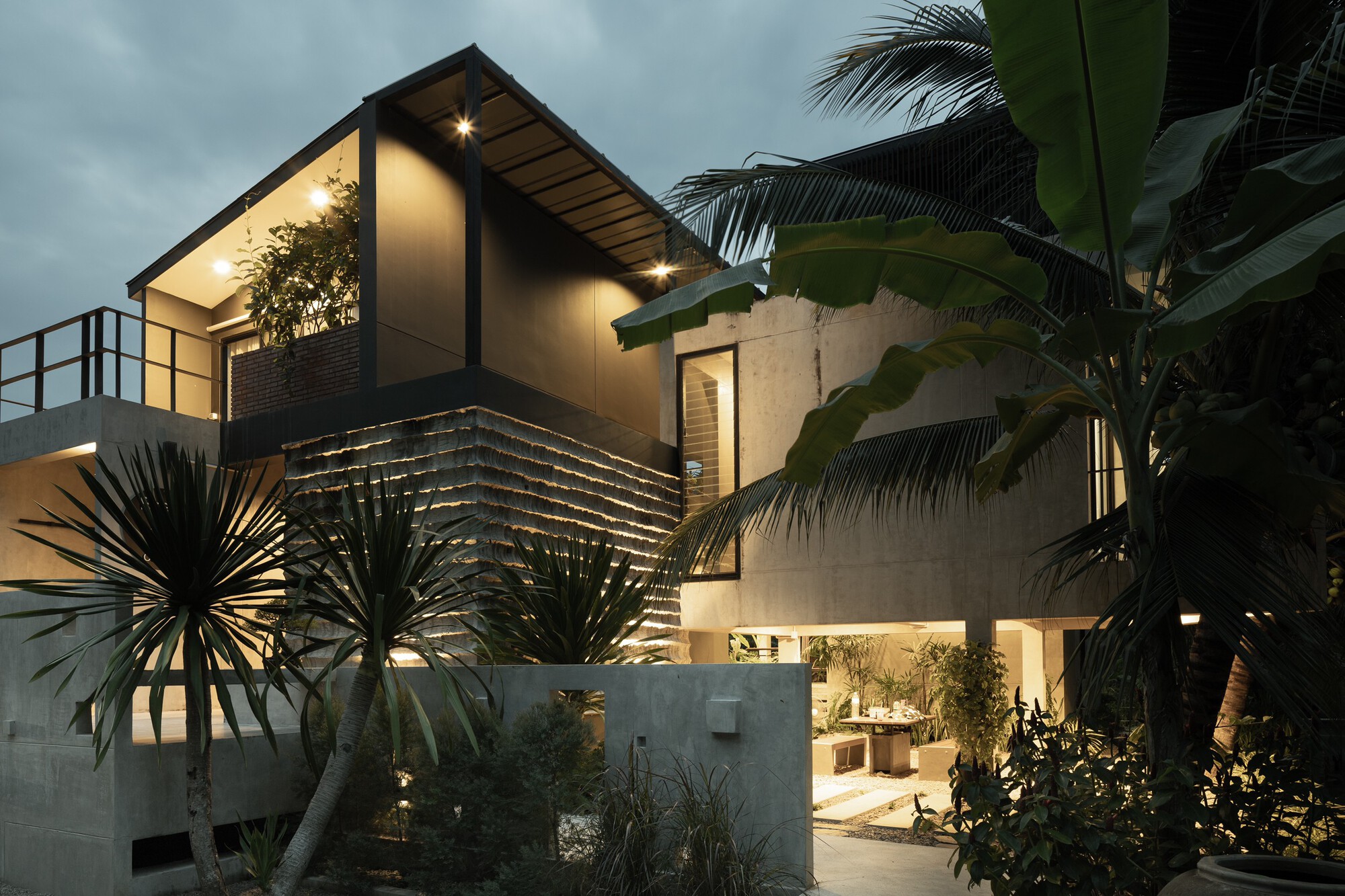 Concrete and timber facade with gabled roof and horizontal slat screening framed by palms at twilight