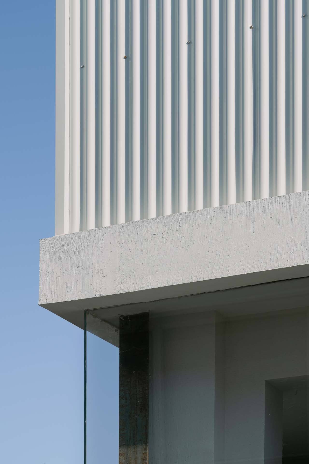 Detail of corrugated cladding meeting a cast concrete edge above a recessed glass opening