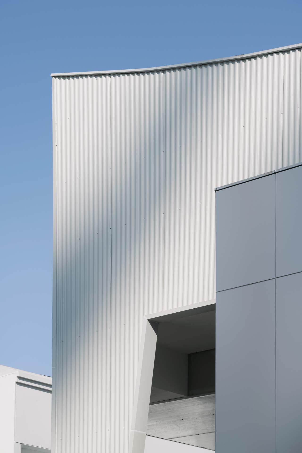Vertical corrugated metal panel rising between flat wall surfaces under a clear blue sky