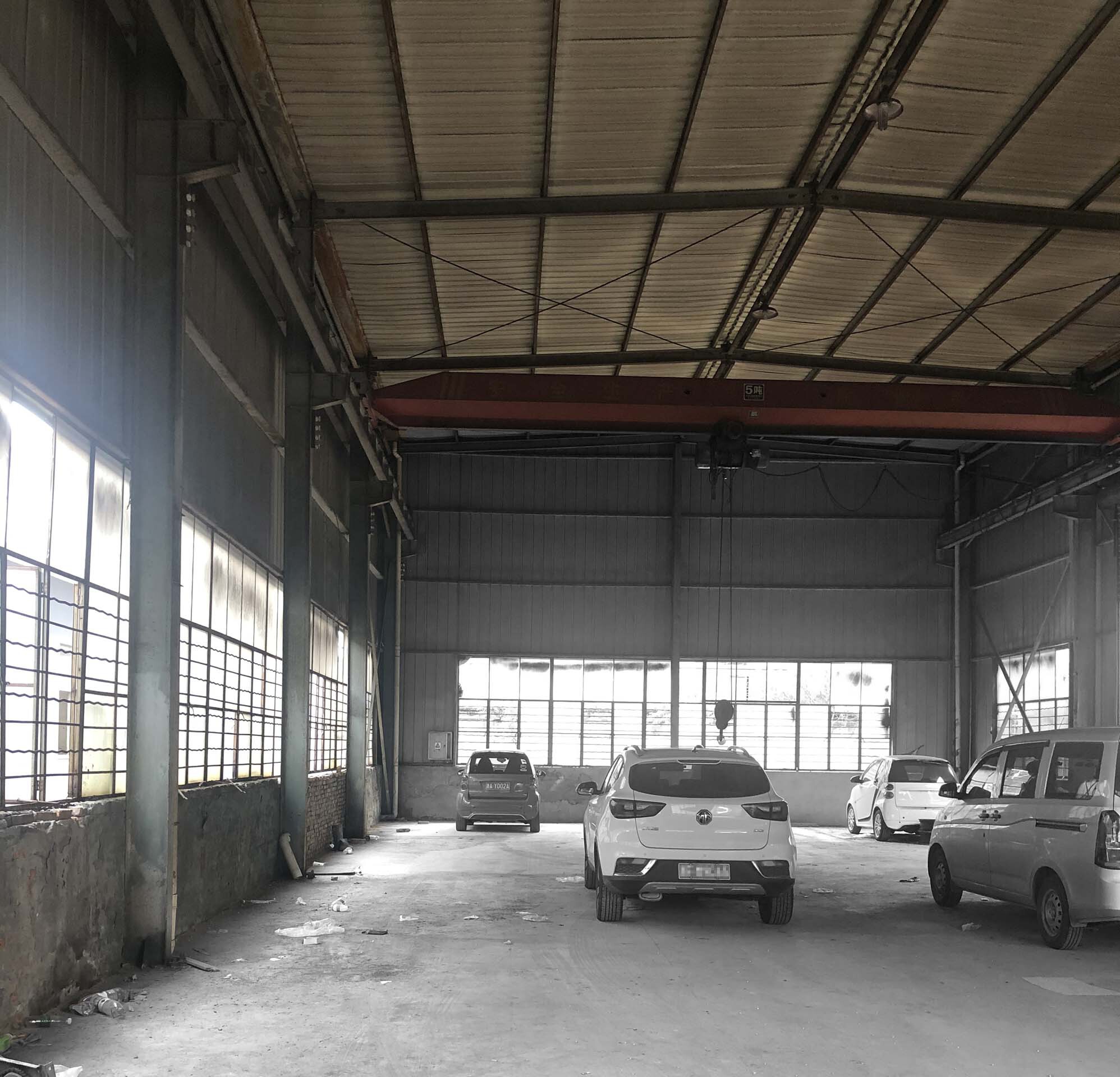 Interior of an industrial hall with exposed steel trusses, gridded windows, and parked vehicles