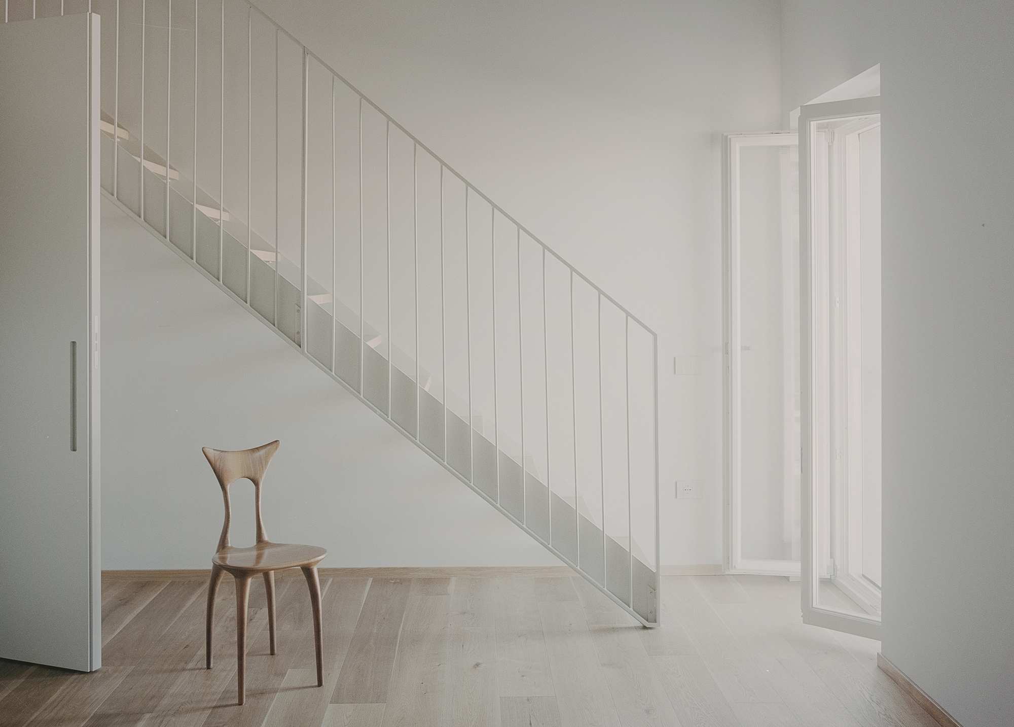 White vertical slatted stair railing with a single wooden chair on light oak flooring